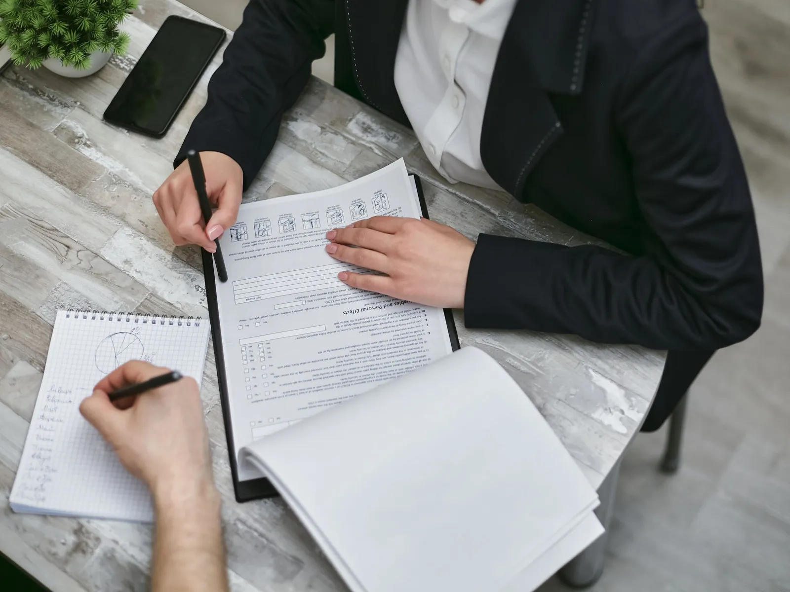 Two colleagues reviewing a form at a desk, one taking notes in a notepad