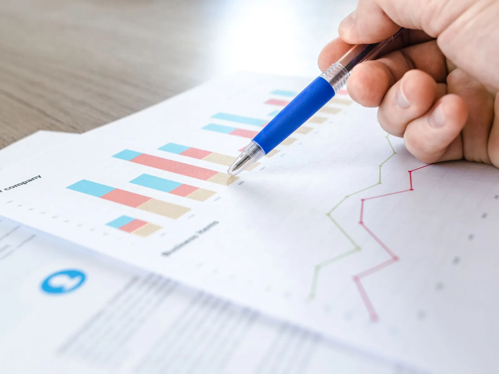 Hand holding a blue pen over printed bar and line charts