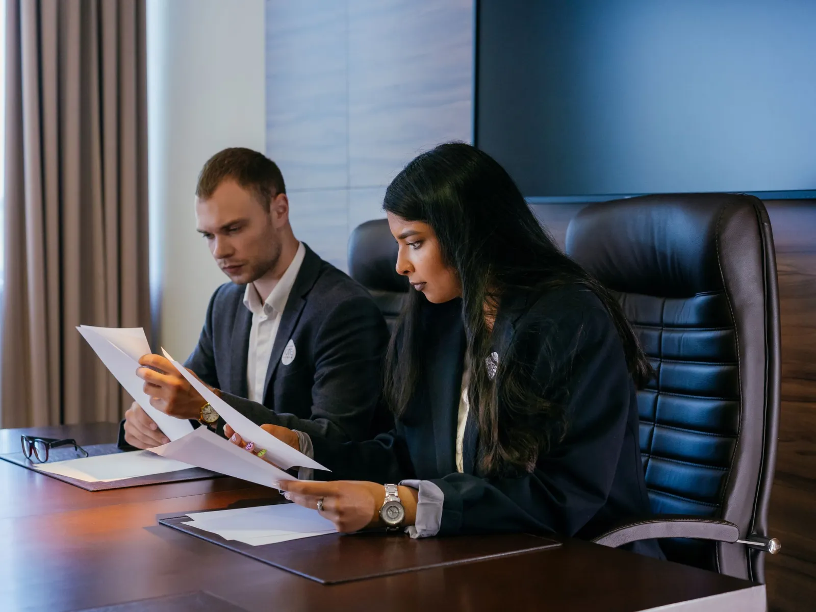 Two professionals reading documents at a dark conference table