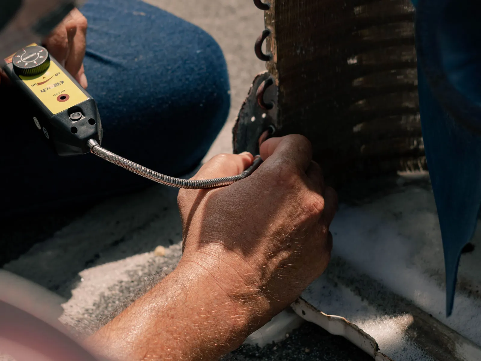 Close-up of a technician using an electronic leak detector on an air-conditioner coil
