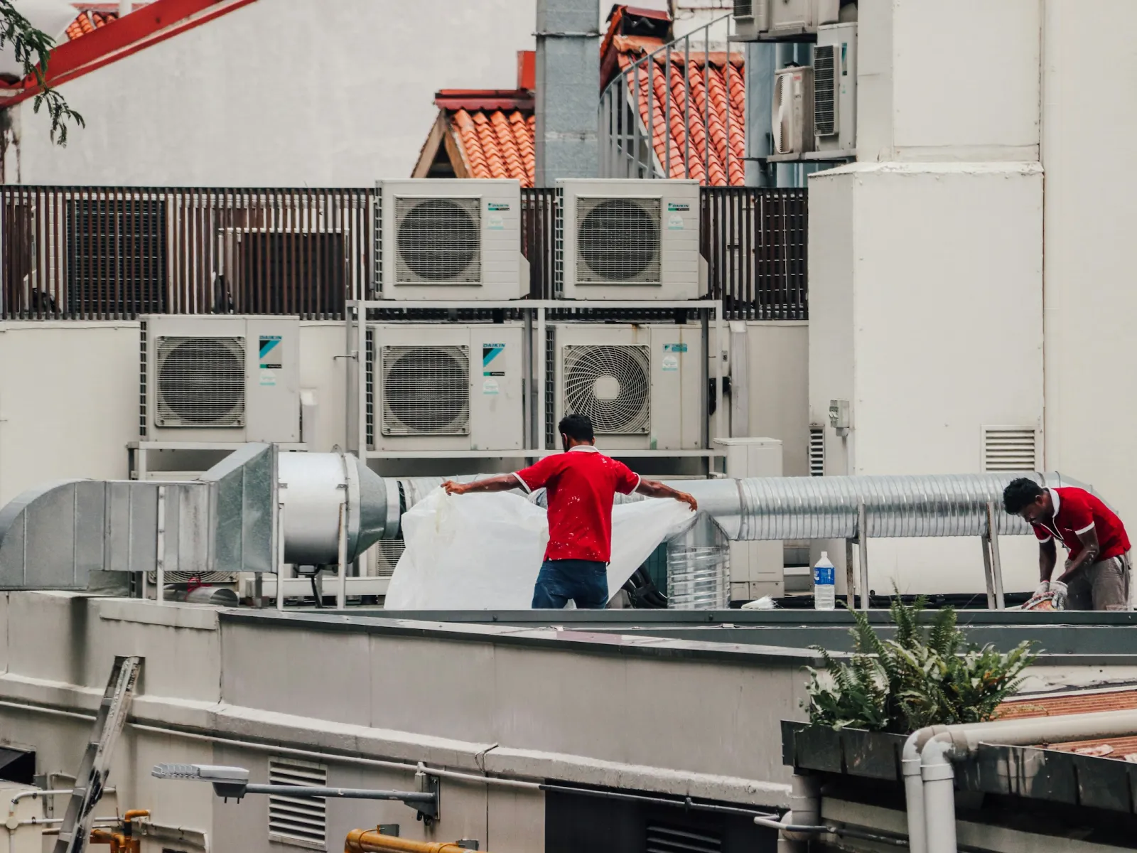 Two technicians working on rooftop ductwork beside banks of outdoor condenser units