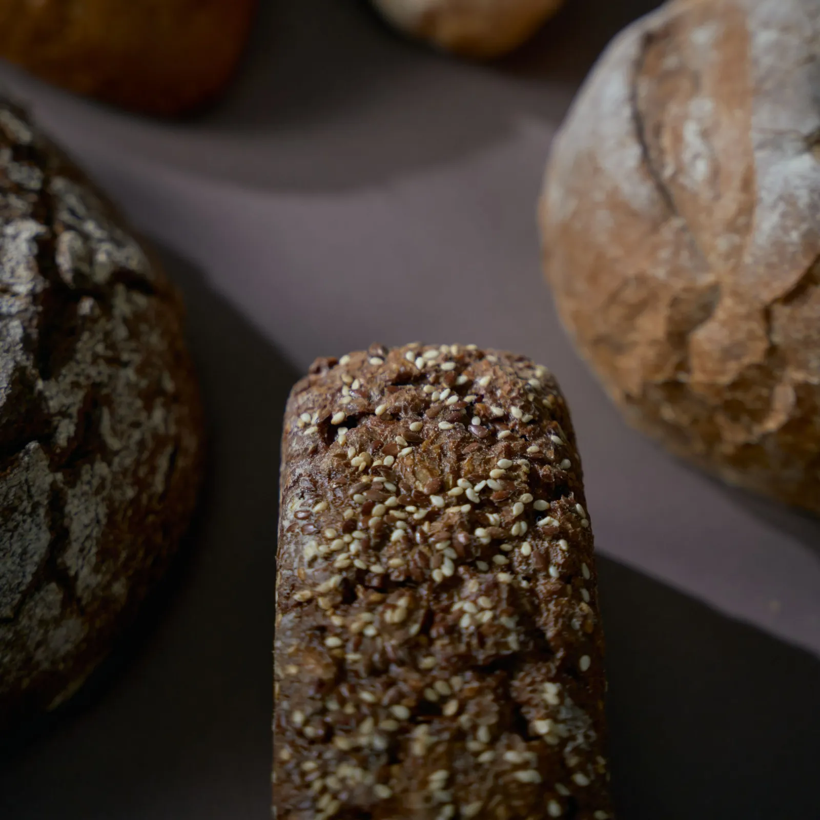 Assorted artisan loaves on a dark table with a seeded rye loaf in sharp focus