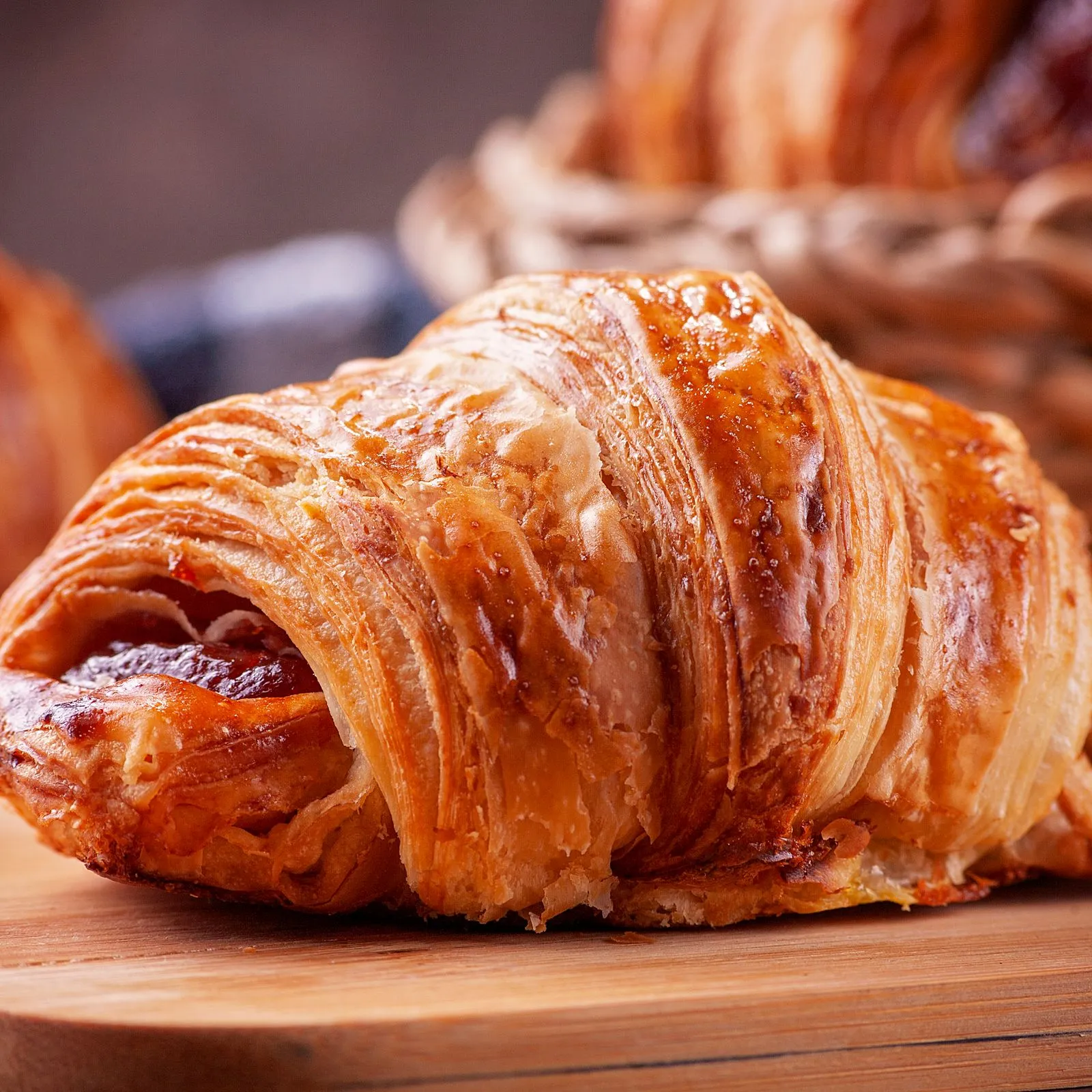 Flaky golden croissant on a wooden board with a bread basket behind