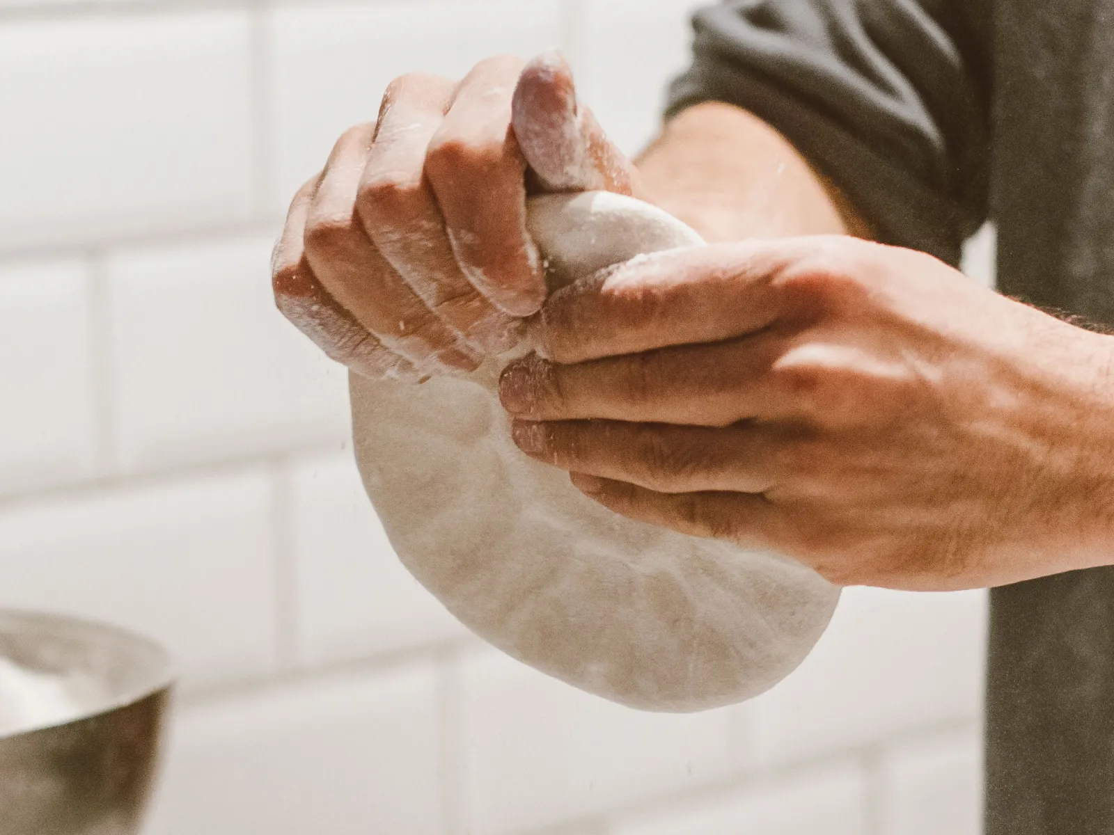 Baker's hands shaping a floured round of dough over a marble counter