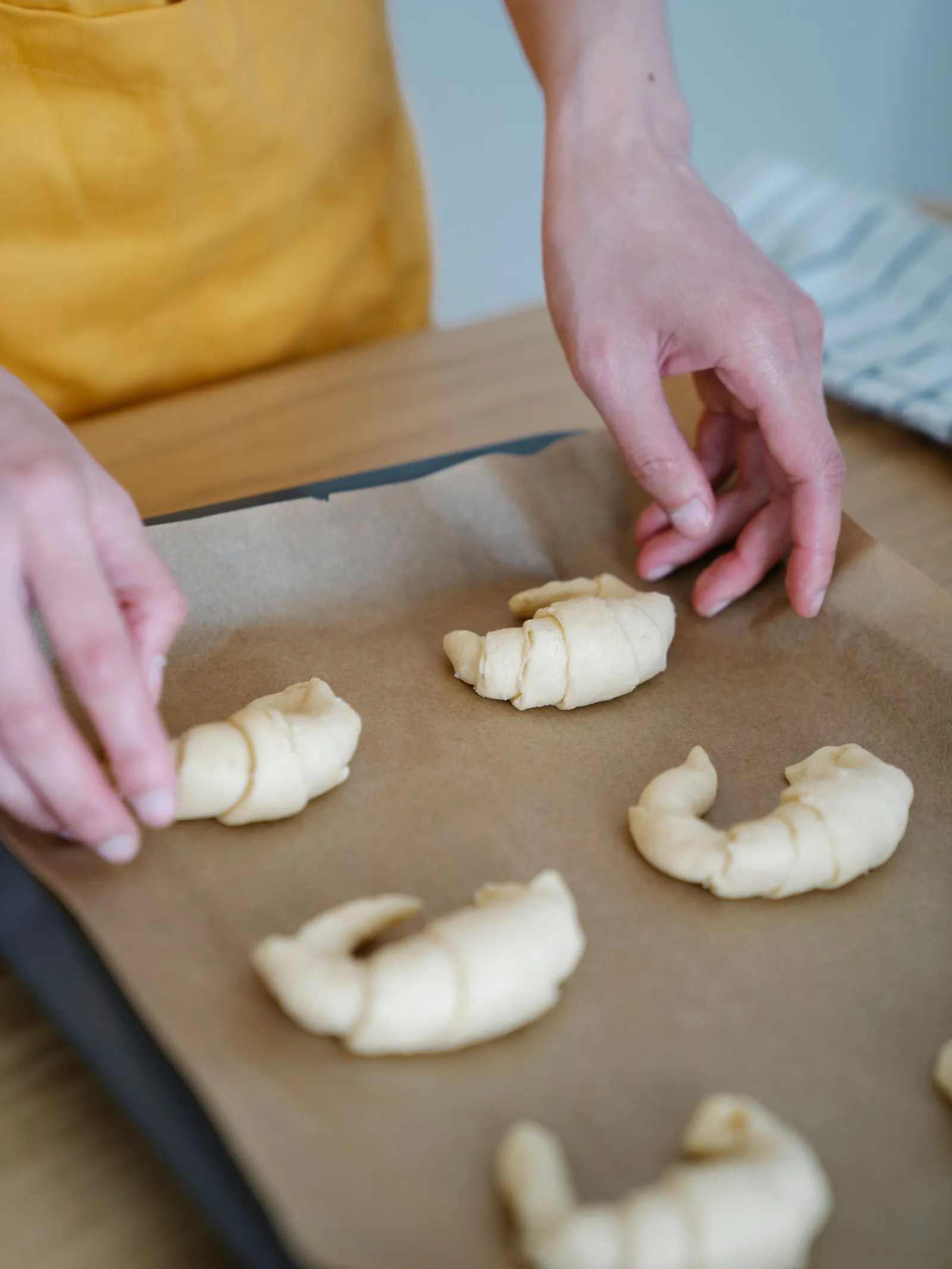 Hands arranging raw croissant rolls on a parchment-lined baking tray