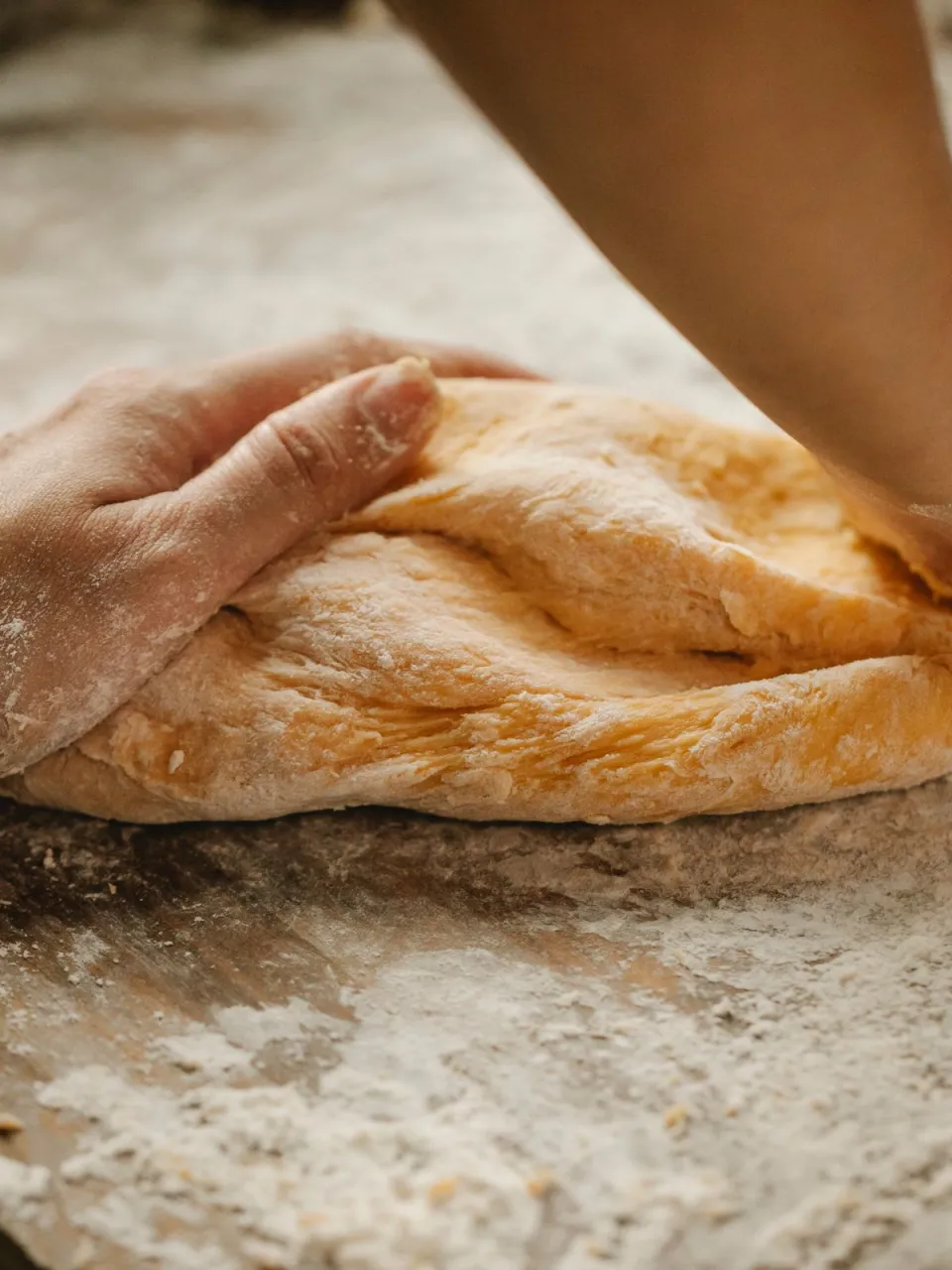 Hands pressing golden dough onto a flour-dusted wooden board
