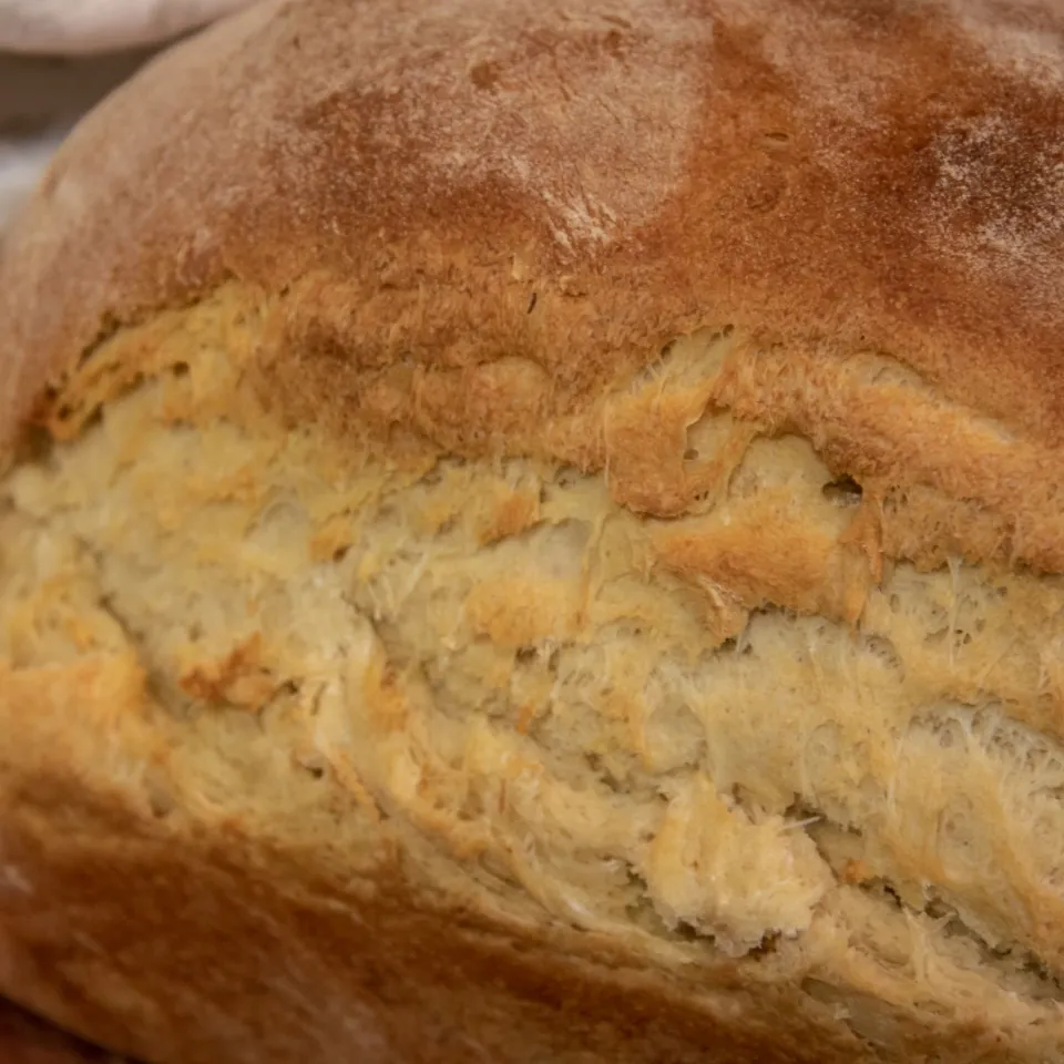 Close-up of a rustic loaf's golden crust beside a patterned linen cloth