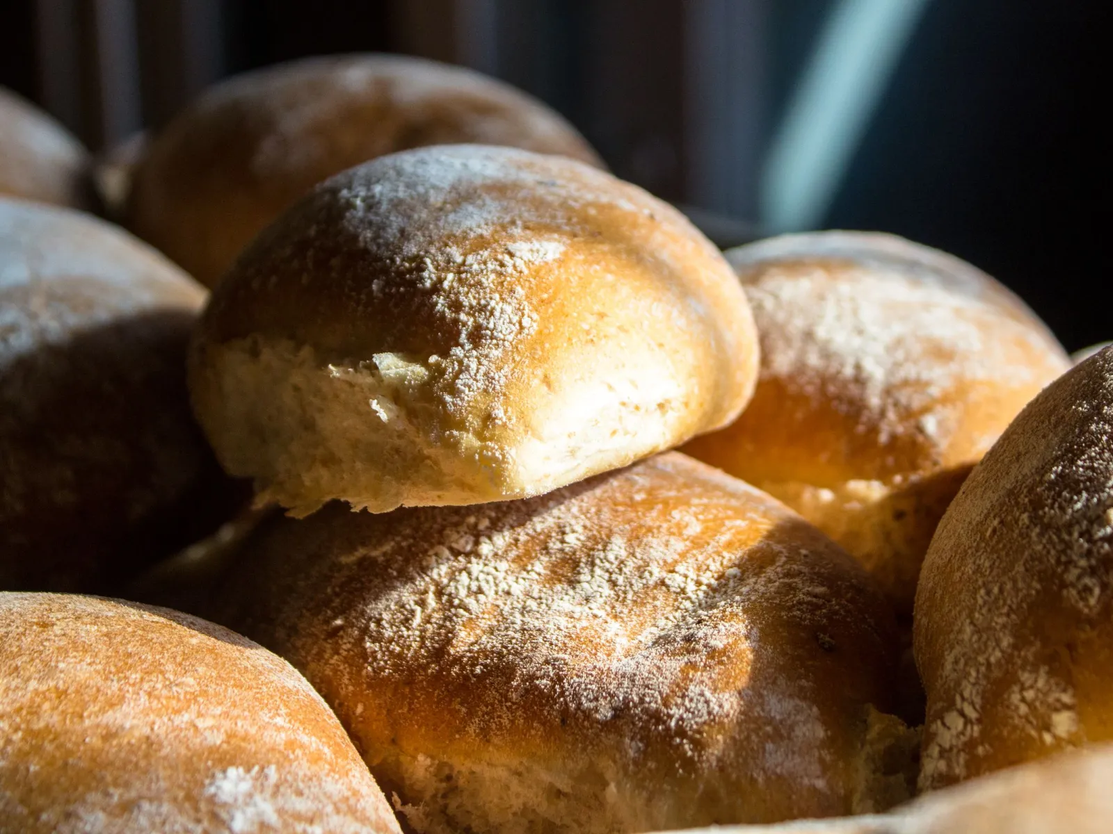 Flour-dusted bread rolls piled in a basket, lit by a beam of warm sunlight