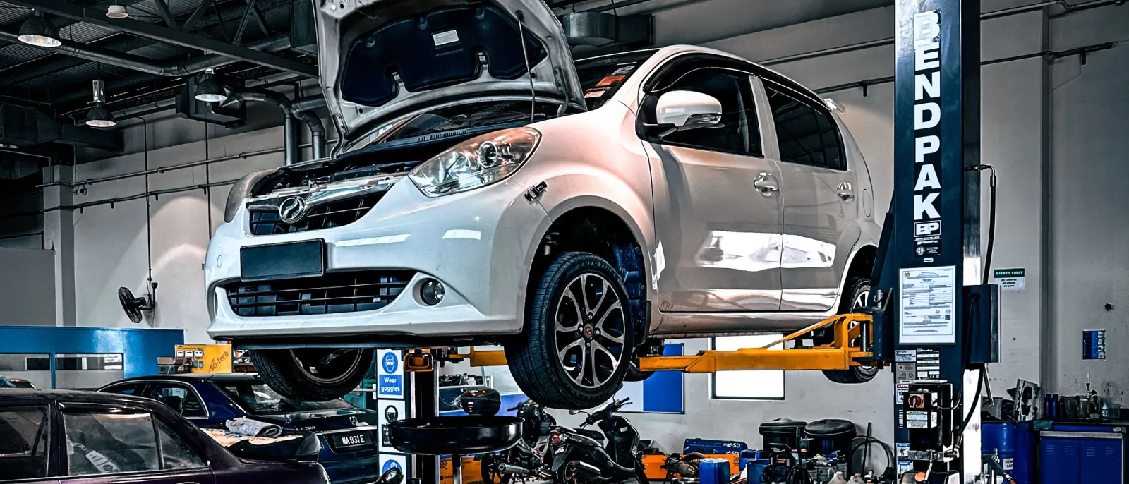 Hatchback with bonnet open raised on a two-post hydraulic lift in a workshop