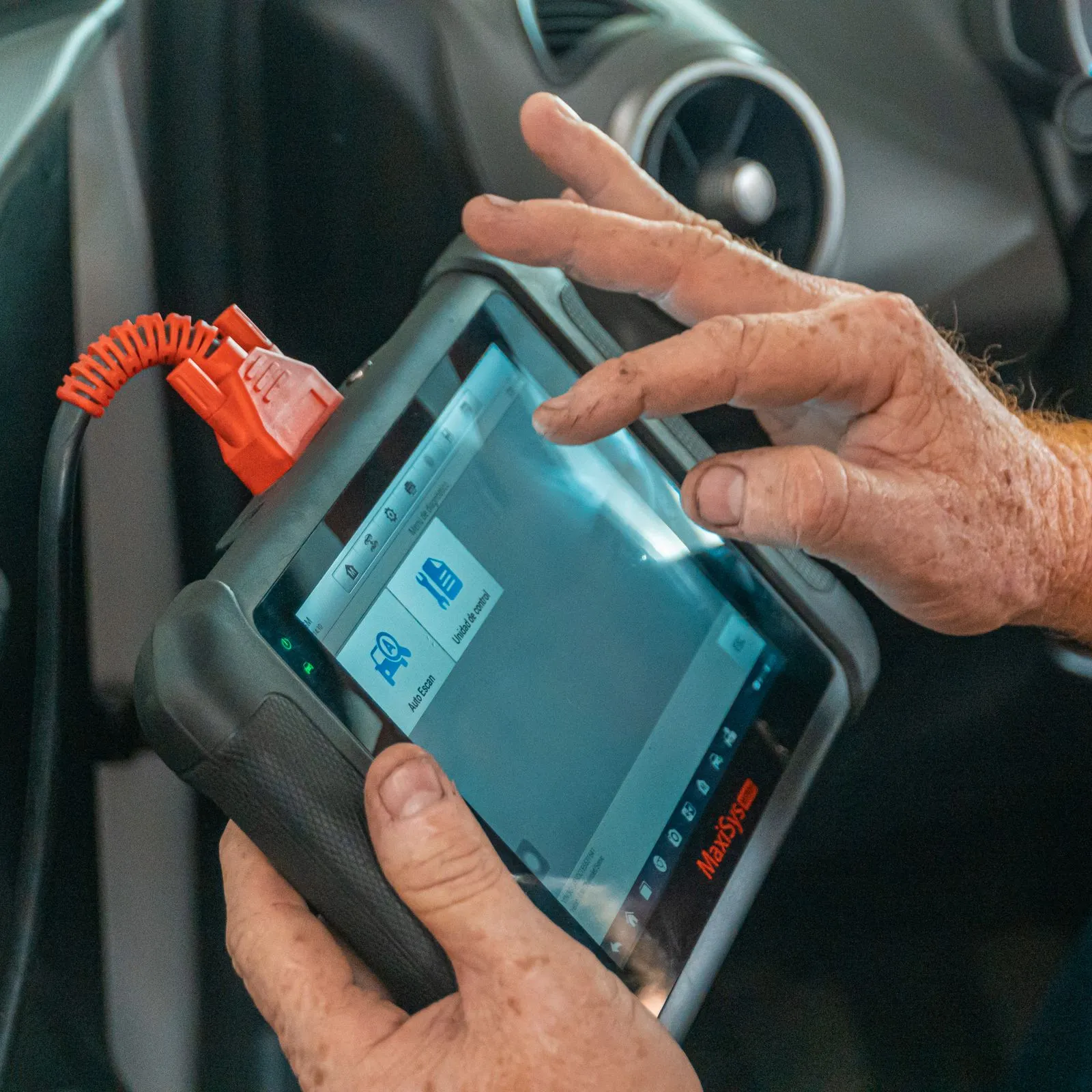 Hands operating a diagnostic tablet connected inside a car cabin