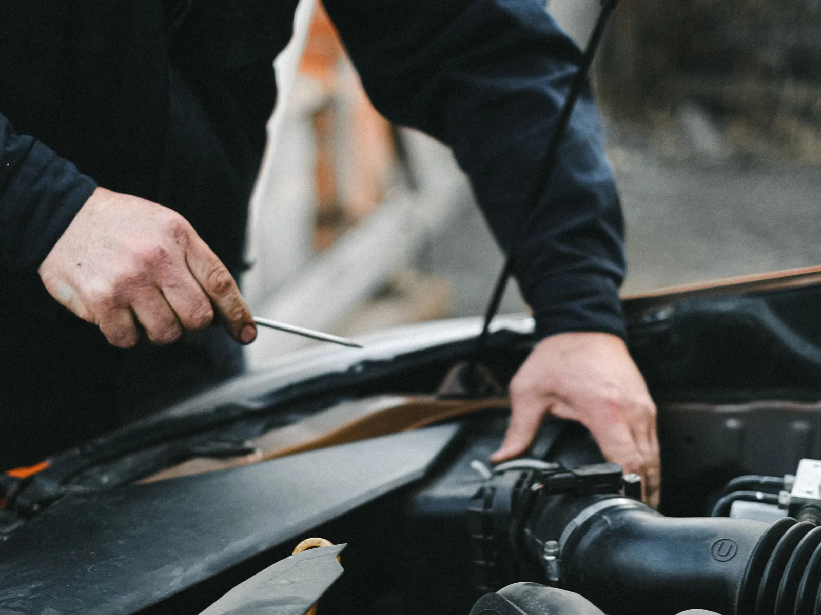 Mechanic's hands working with a dipstick over a dark engine bay