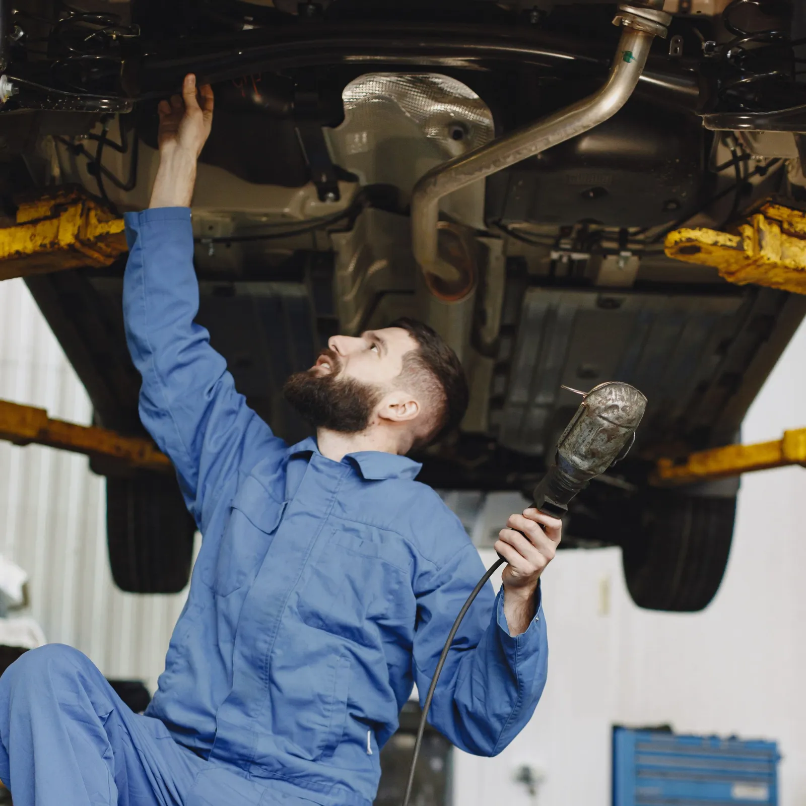 Mechanic with an inspection lamp checking the underside of a car on a lift