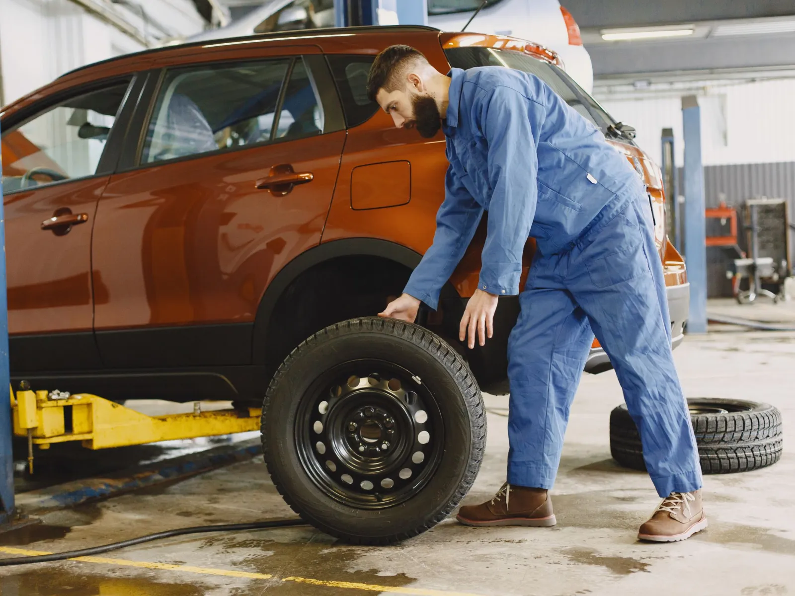 Mechanic rolling a fresh wheel to an orange SUV raised in a tyre bay