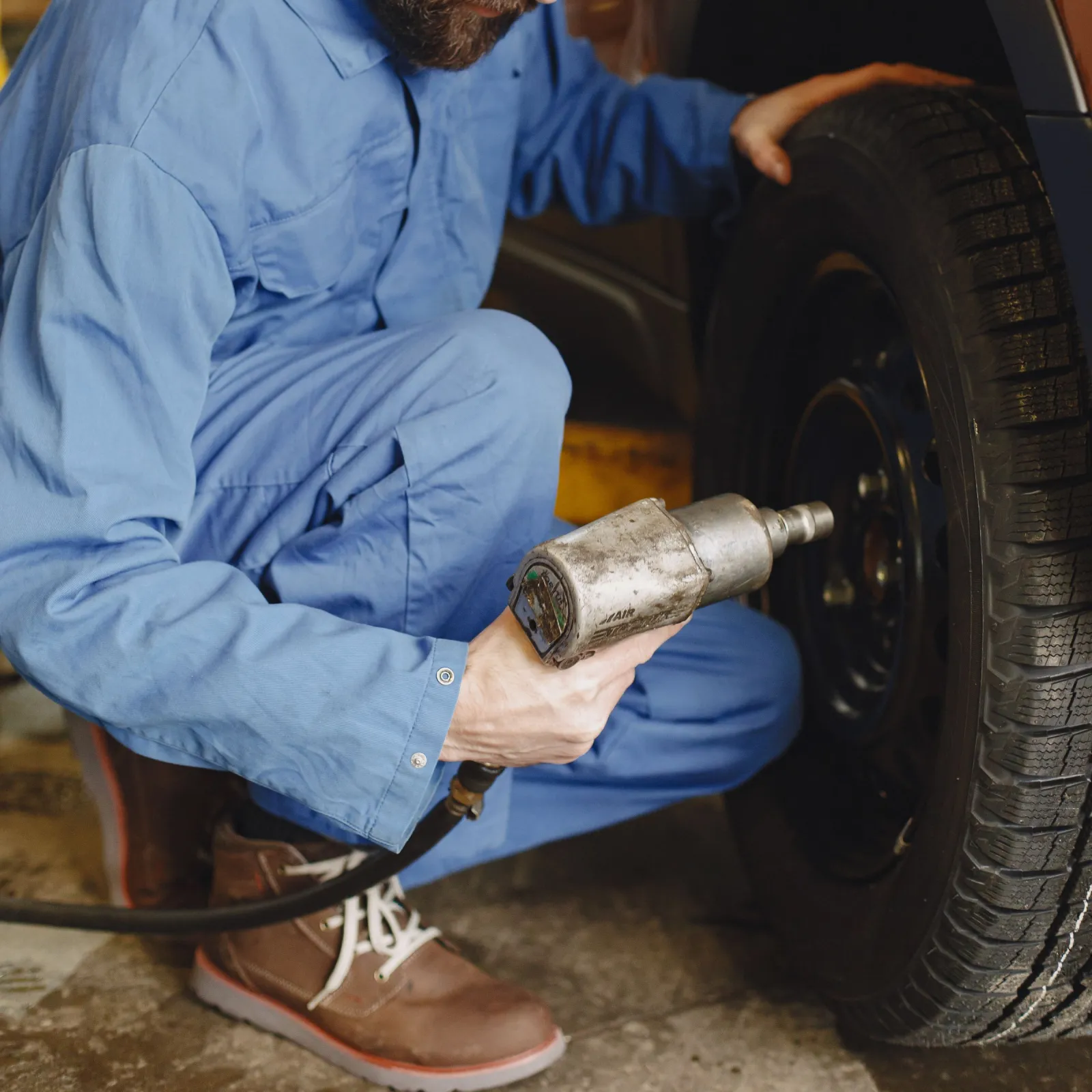 Mechanic tightening wheel nuts with an air impact wrench during a tyre change
