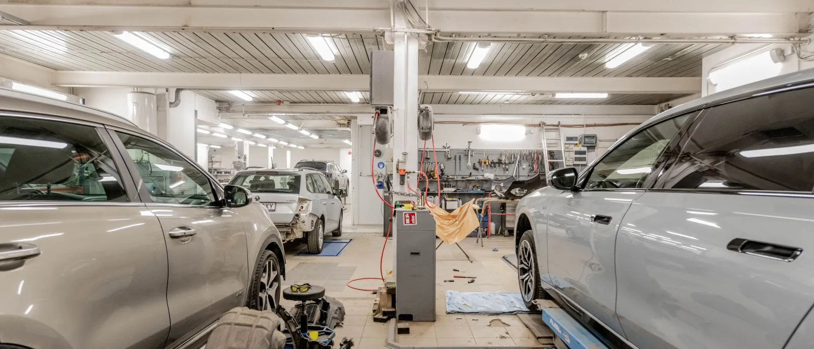 Service bays with two cars and a tool wall inside a bright car workshop