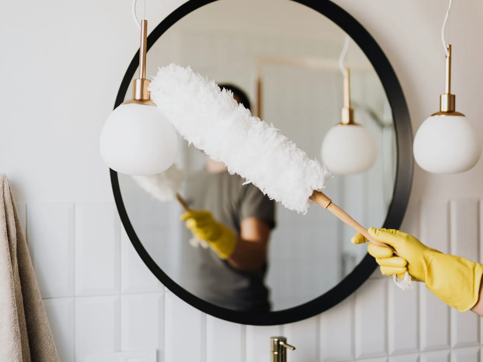 Yellow-gloved hand dusting a pendant lamp in front of a round mirror