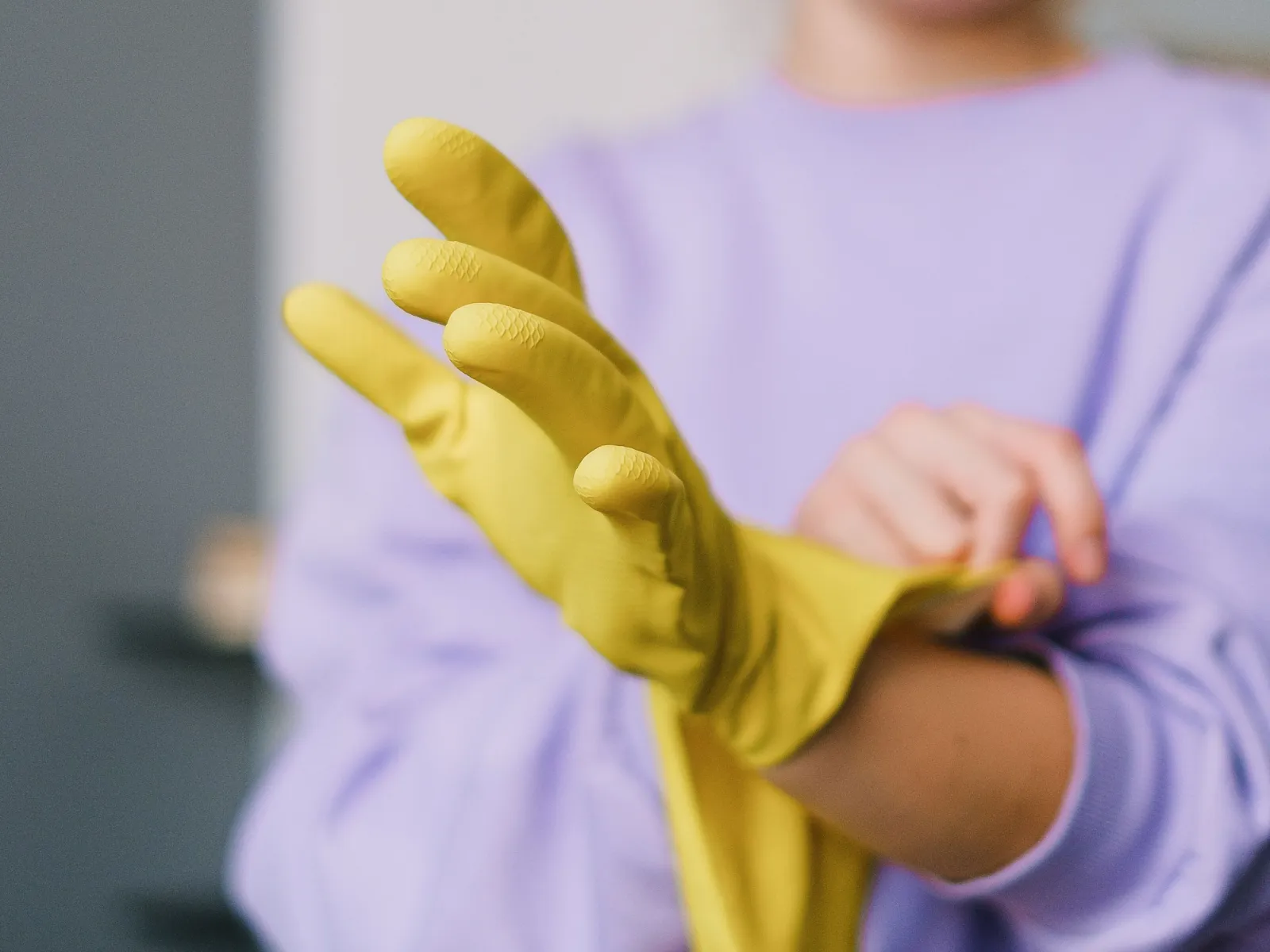 Cleaner in a lavender sweater pulling on yellow rubber gloves