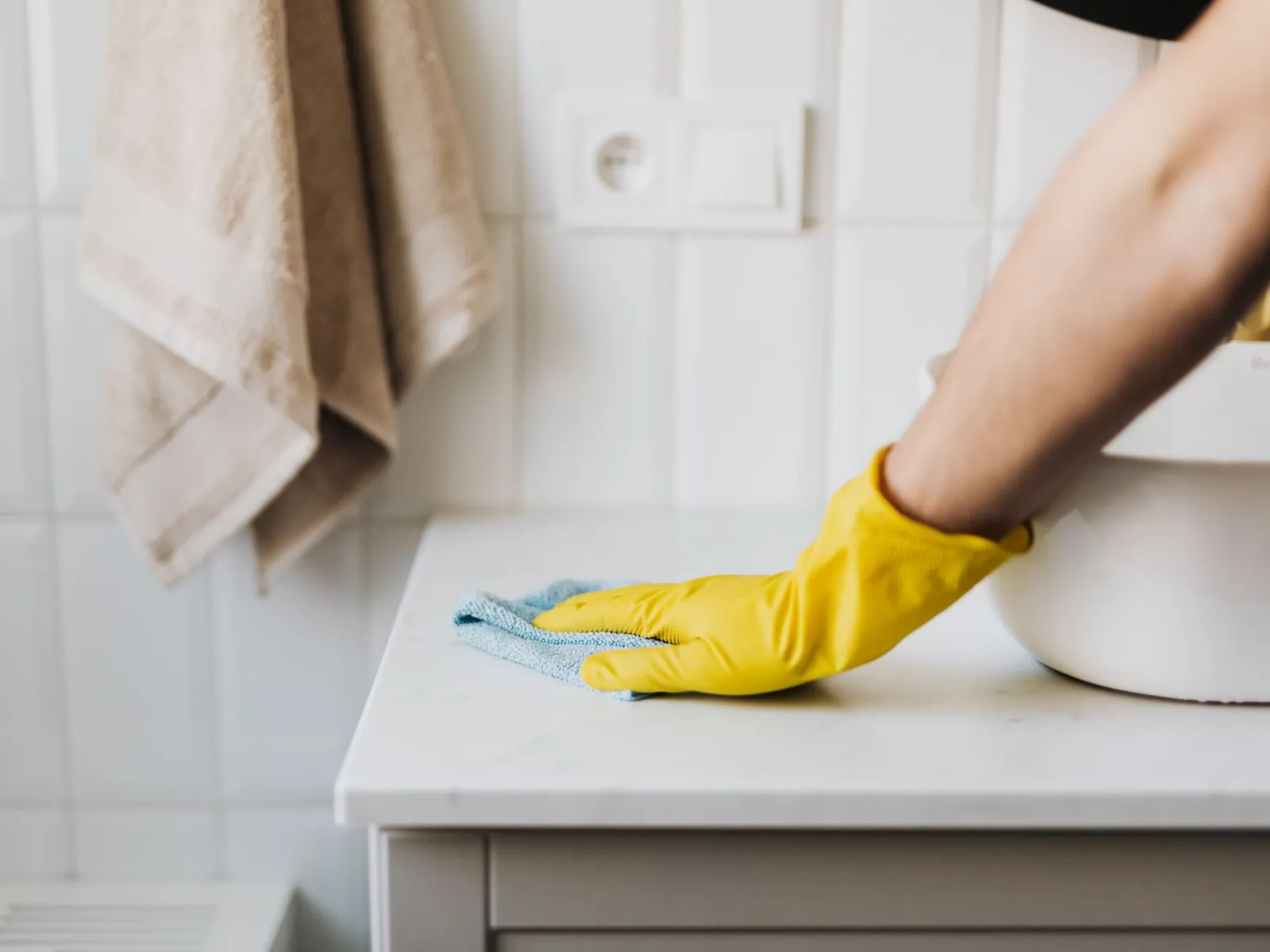 Hand in a yellow rubber glove wiping a white counter with a blue microfiber cloth