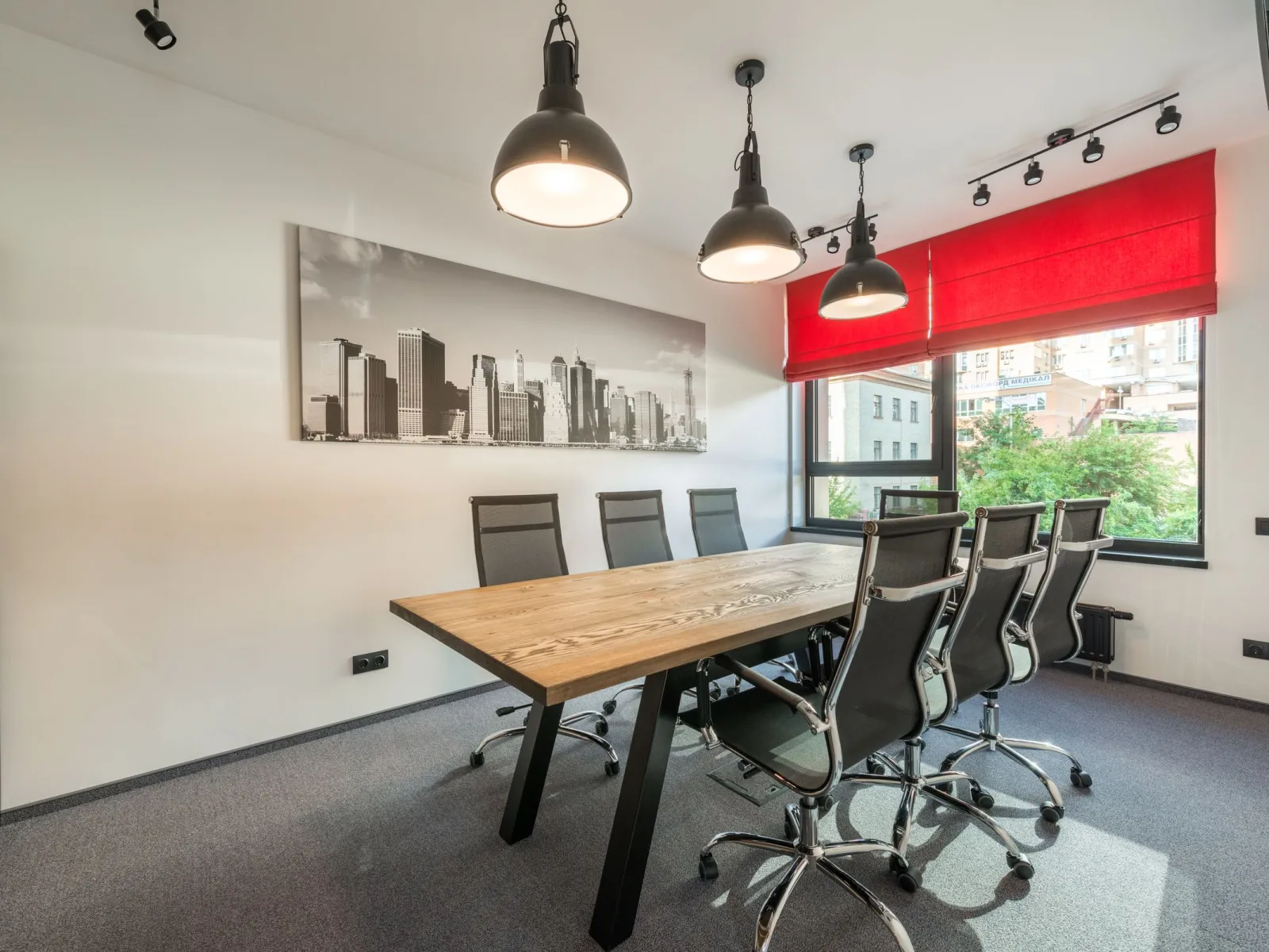 Industrial meeting room with wooden table, black mesh chairs, pendant lamps and red blinds