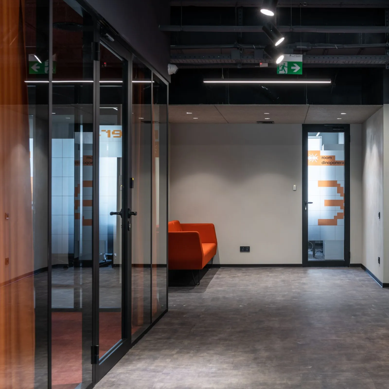 Orange sofa in a dim coworking corridor lined with glass-walled meeting rooms