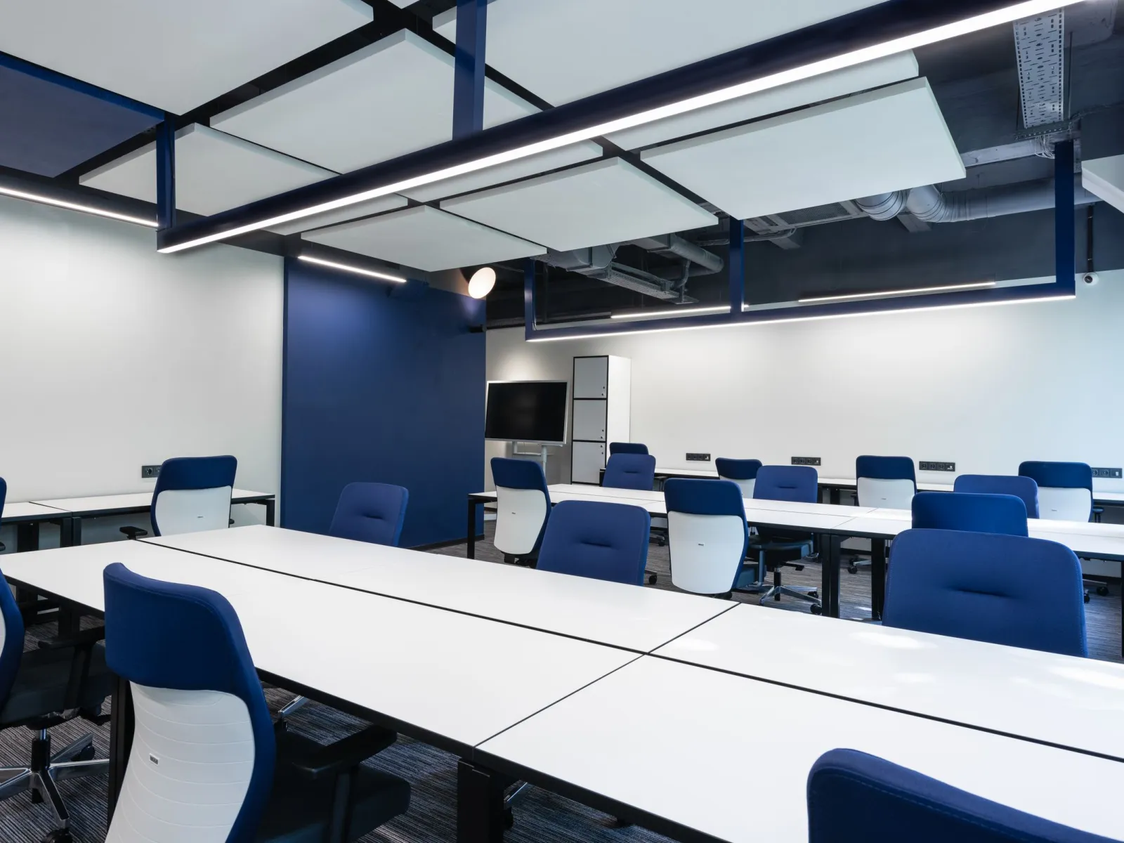 Open-plan coworking area with long white desks, blue task chairs and linear pendant lighting