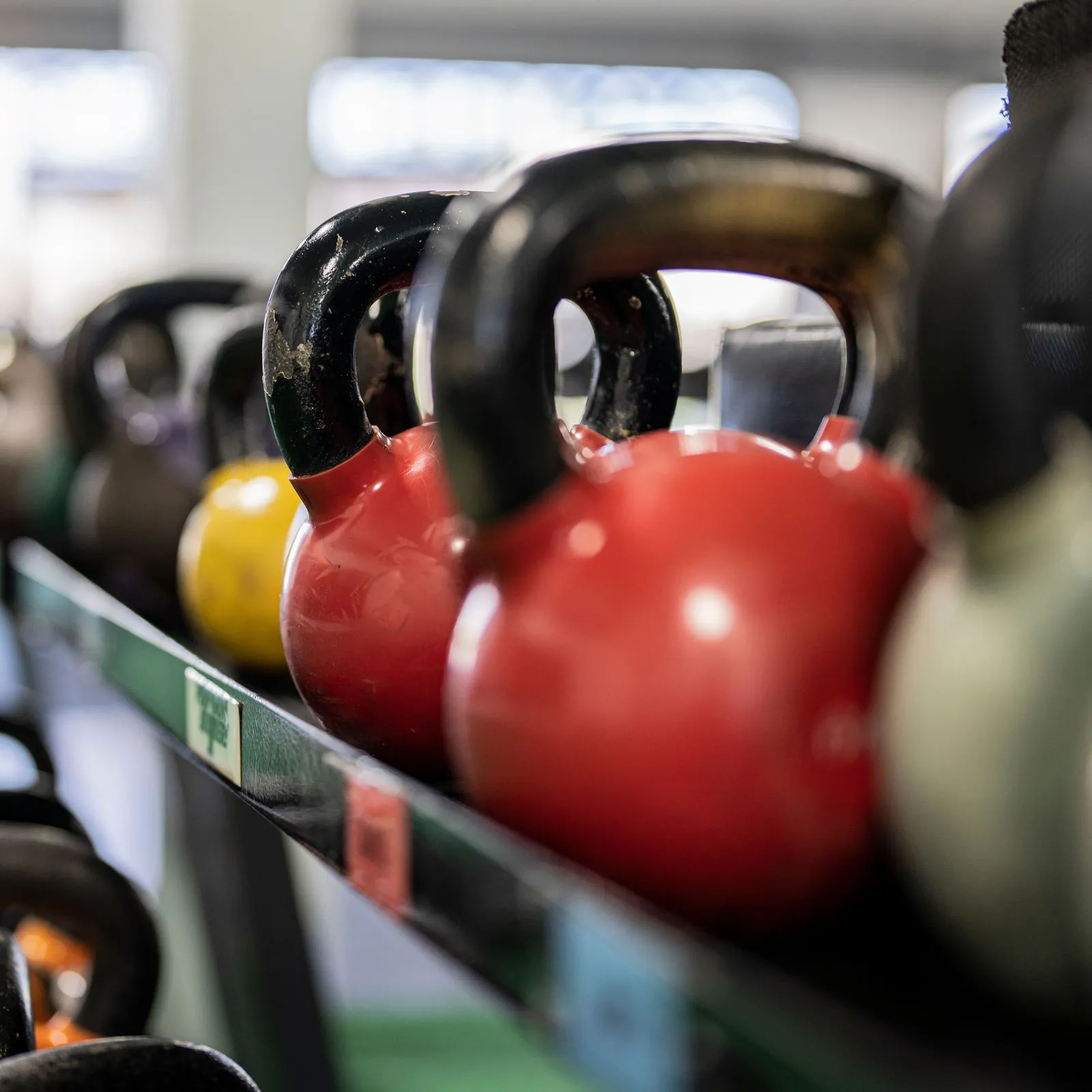 Row of red and black kettlebells lined up on a rack in a sunlit gym