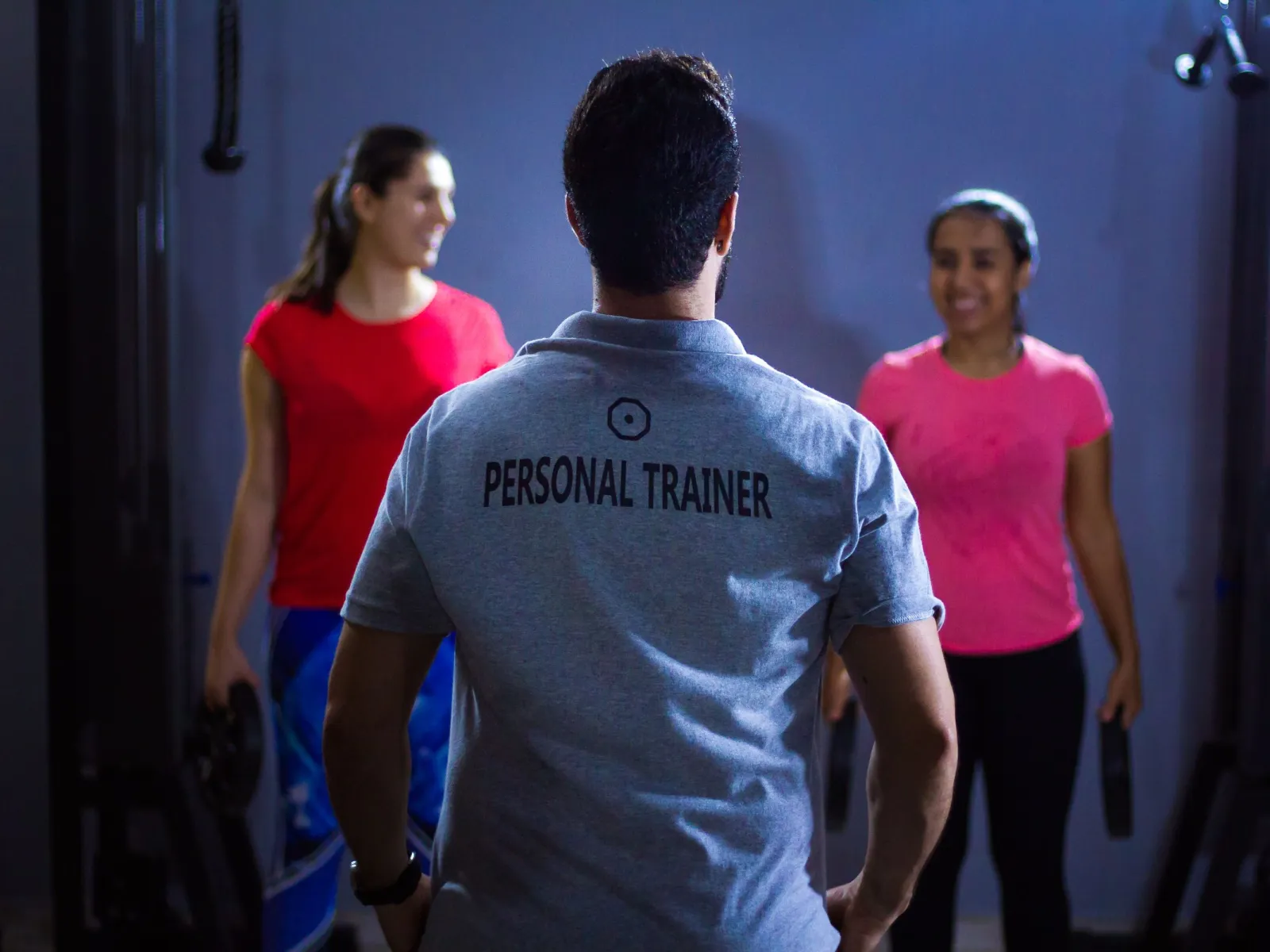Personal trainer seen from behind facing two clients holding weight plates in a gym