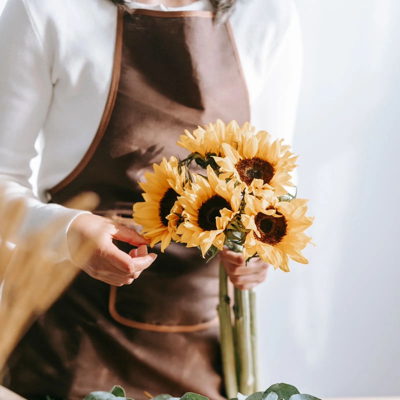 Florist in a brown apron gathering a sunflower bunch above eucalyptus greenery