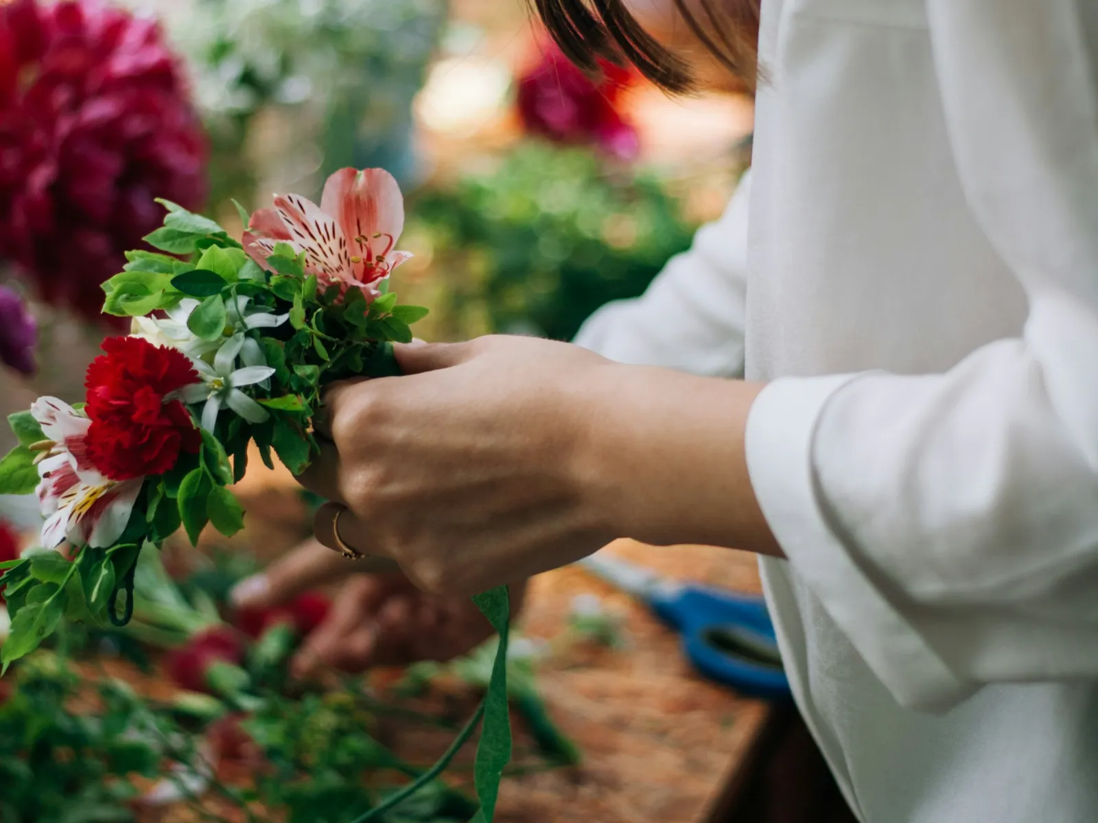 Florist's hands binding a red carnation posy with green floral tape at a workbench