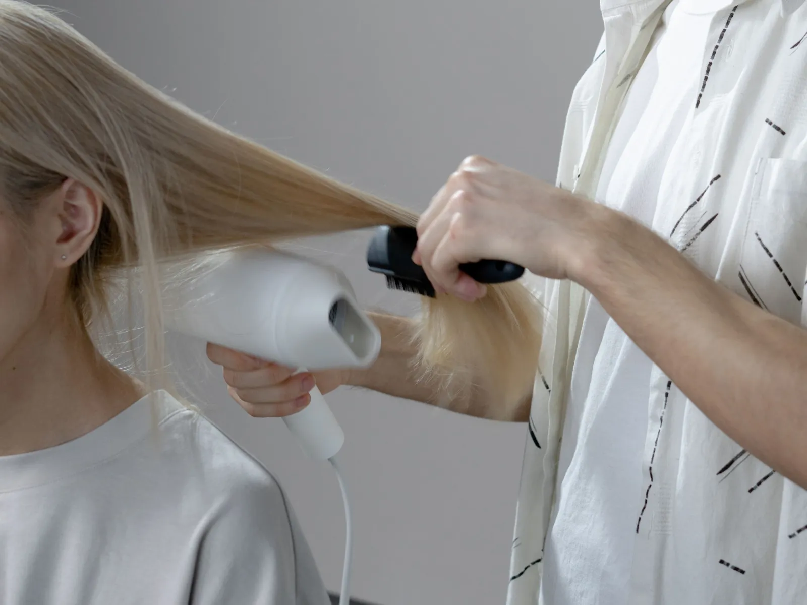 Stylist blow-drying a client's long blonde hair with a round brush