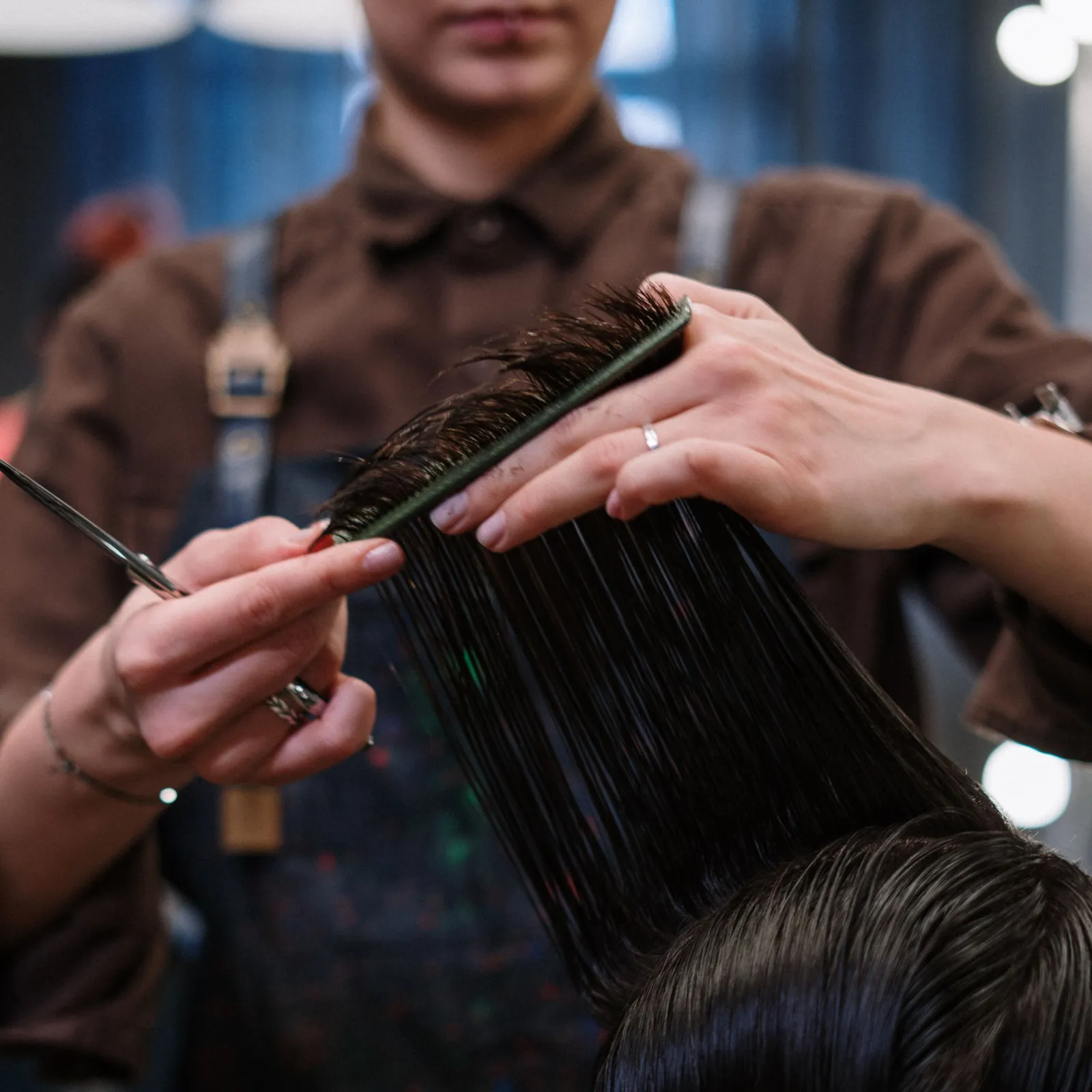 Stylist sectioning a client's wet dark hair with a comb before cutting