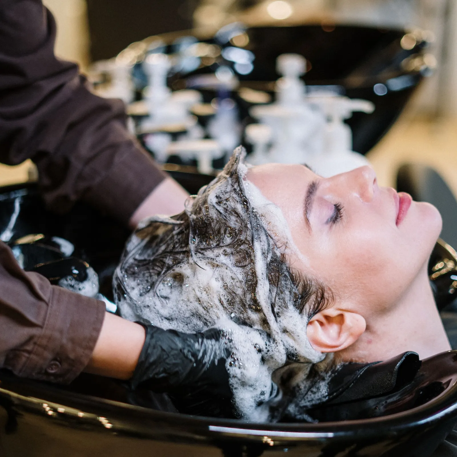 Client relaxing while having her hair shampooed at a black salon basin