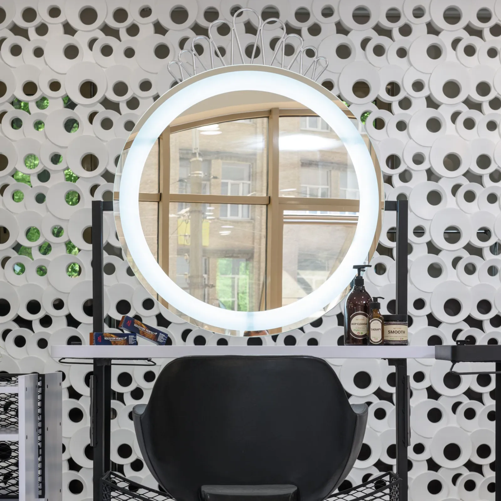 Salon workstation with an illuminated round mirror, black chair, and hair care products