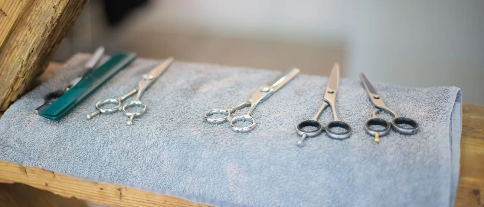 Hairdressing scissors and a comb laid out on a folded towel on a wooden bench