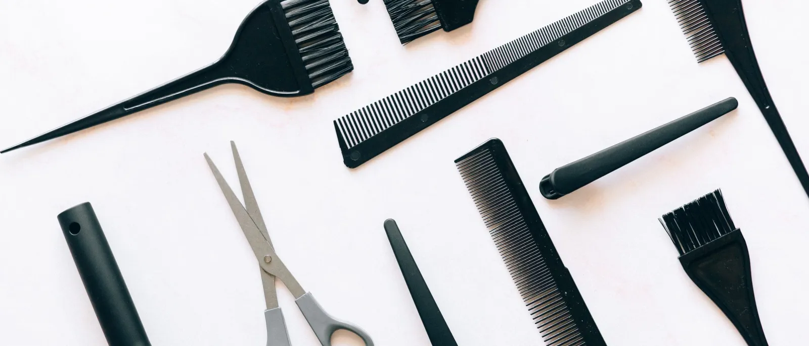 Flat lay of black hairdressing combs, tint brushes, and scissors on a white surface
