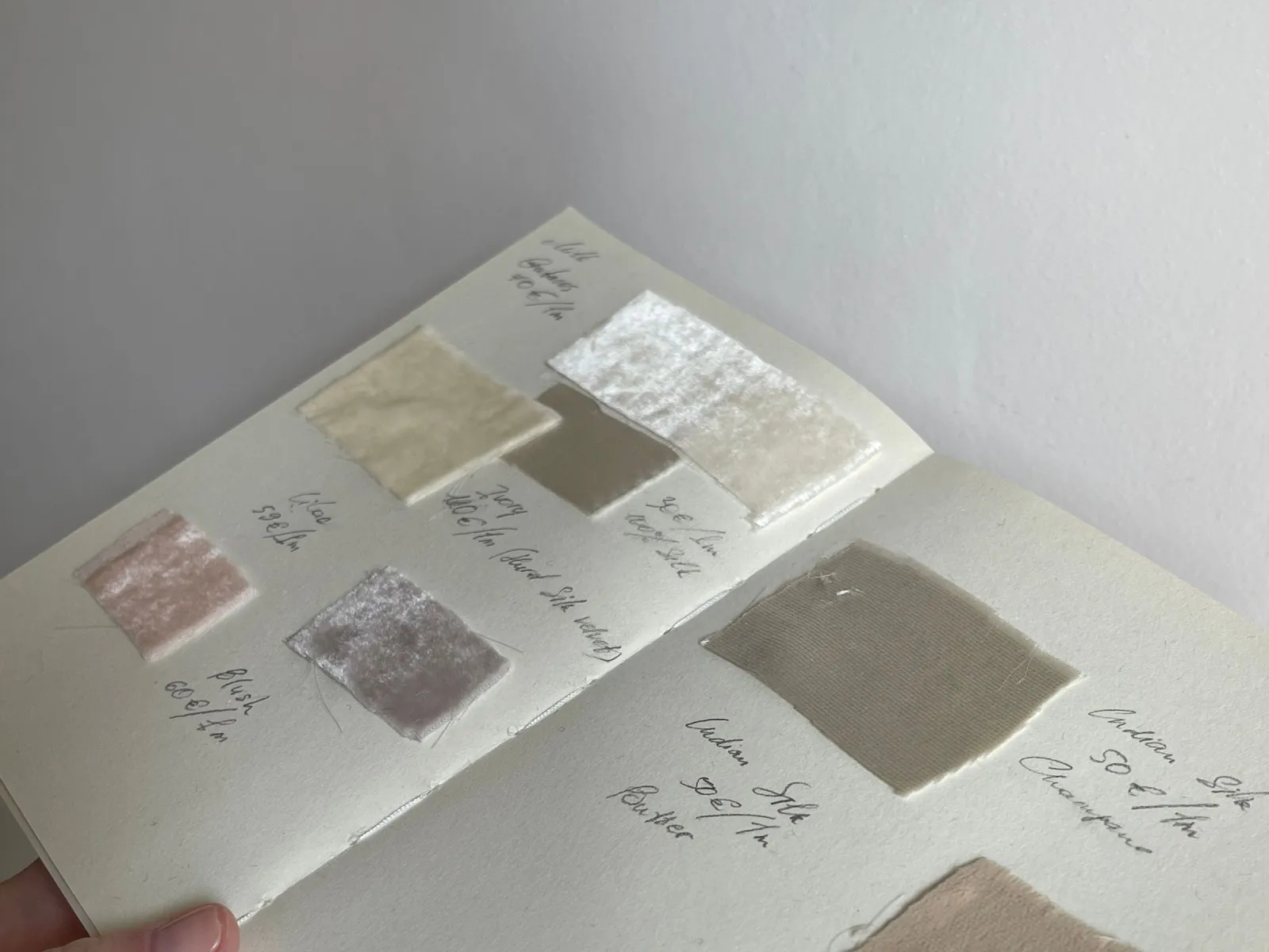 Hand holding an open notebook with velvet and silk fabric swatches and handwritten notes