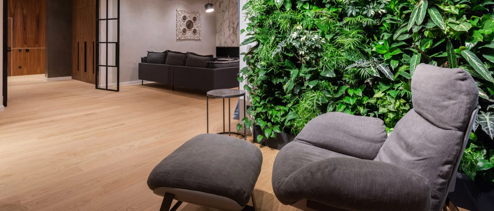 Modern lounge with floor-to-ceiling living plant wall and gray upholstered armchair with footstool