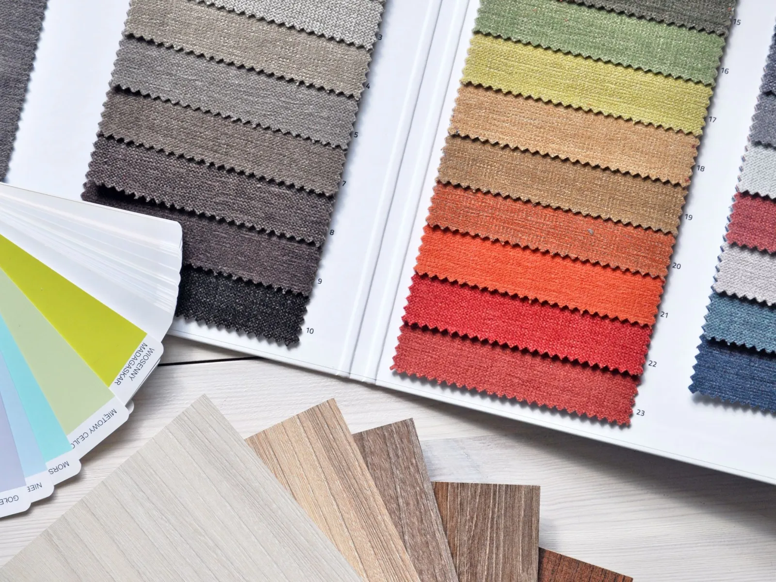Fabric sample books, a paint color fan deck and wood flooring swatches spread on a white table