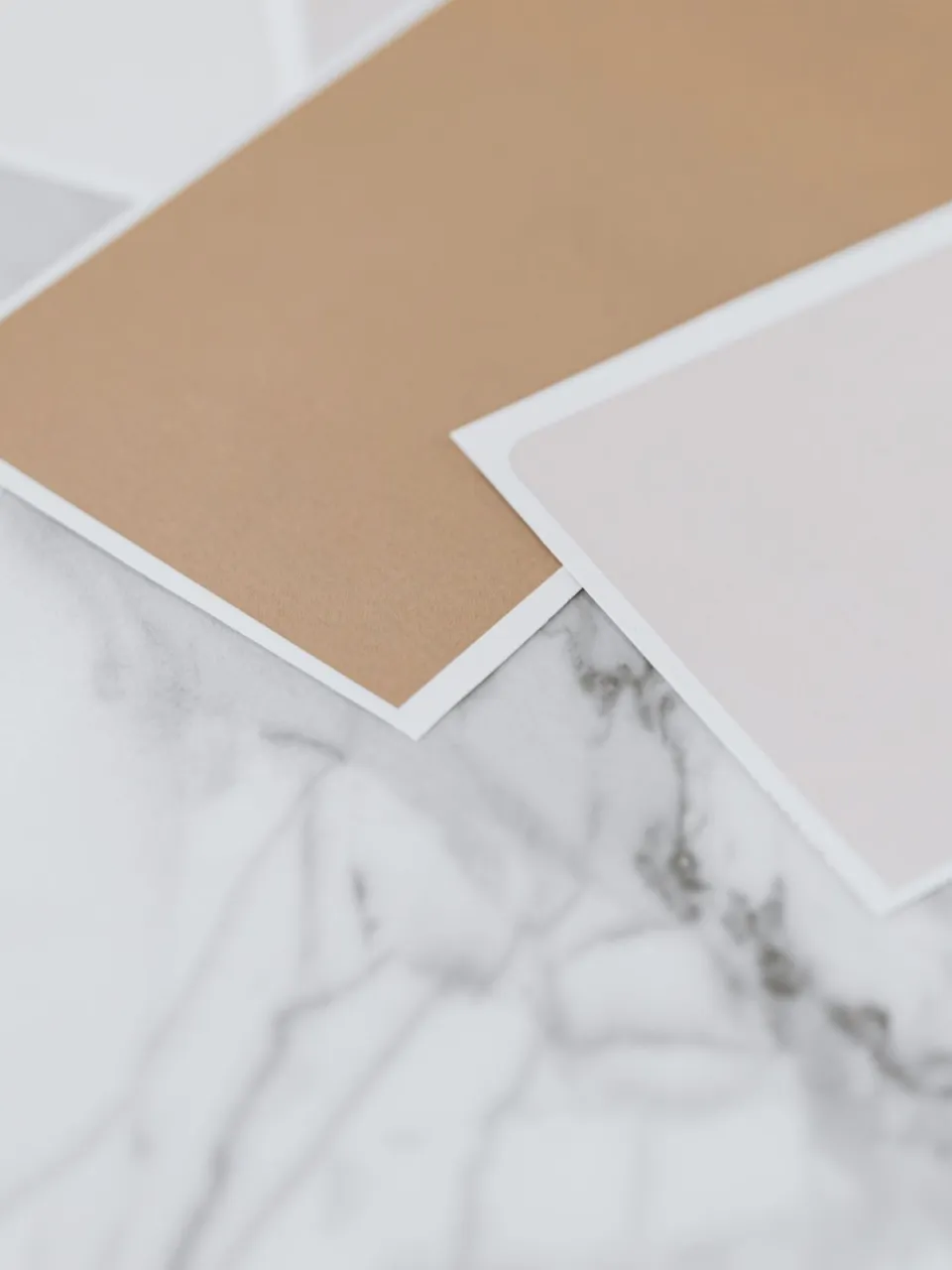 Neutral beige and taupe paint sample cards fanned out on a white marble surface