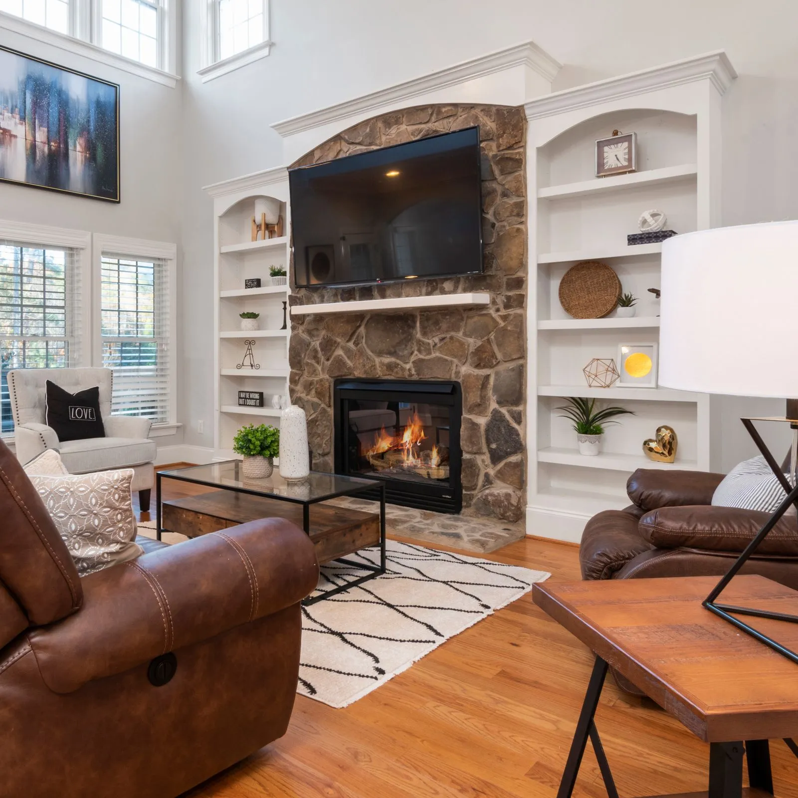 Living room with stone fireplace, built-in white shelves and brown leather sofas