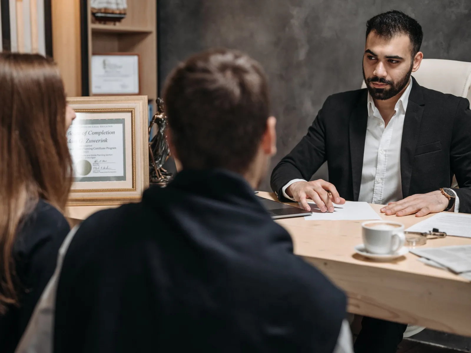 Lawyer at a wooden desk reviewing paperwork with two clients seated across from him