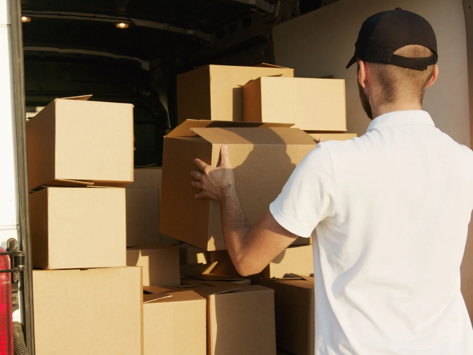 Courier seen from behind loading a cardboard box into a van full of parcels