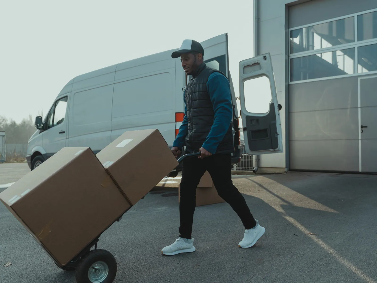 Courier pushing a hand trolley with large boxes from a van toward a loading bay