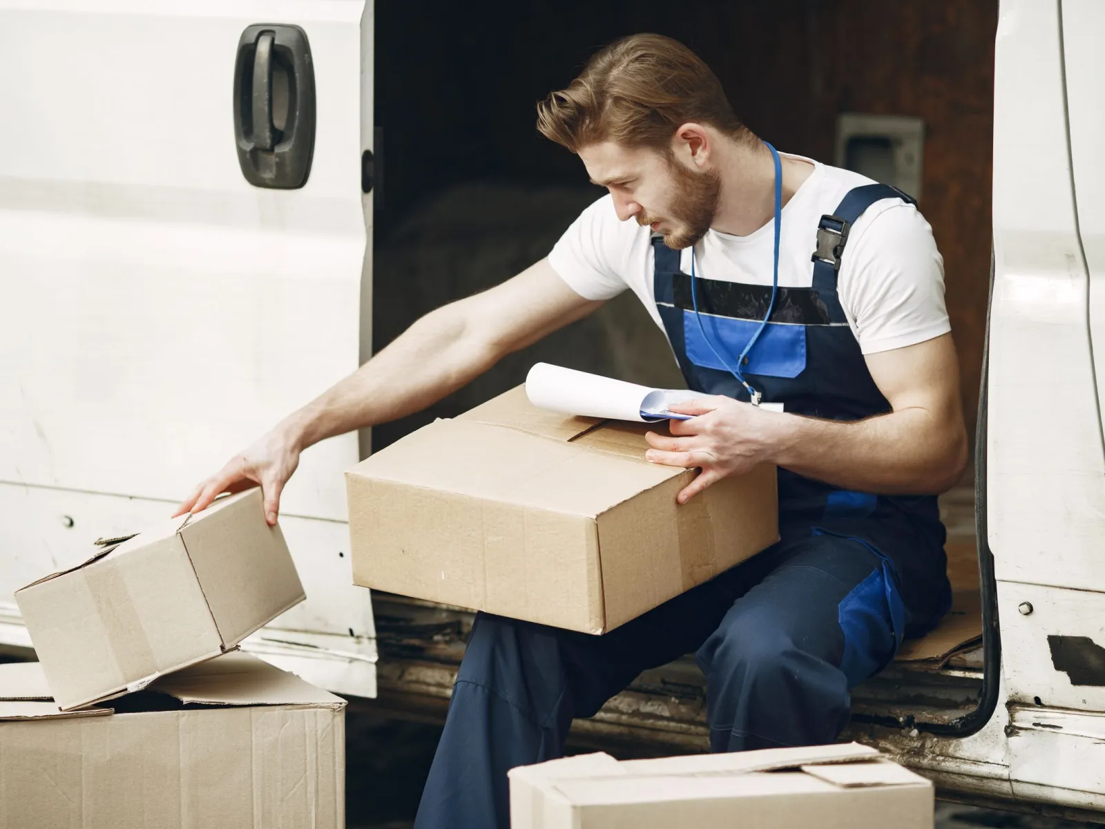 Delivery worker seated at the back of a van checking paperwork on a parcel