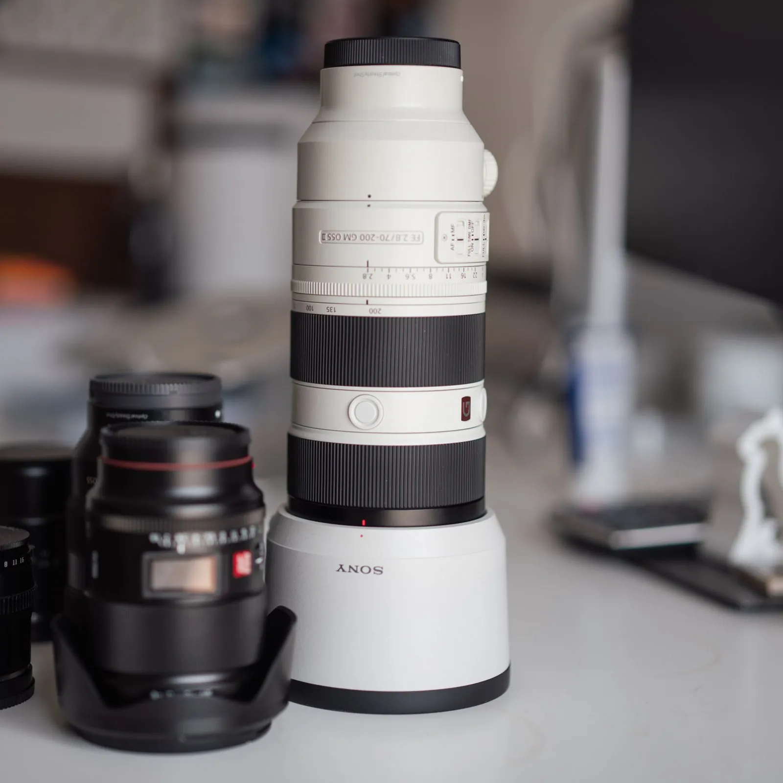 White telephoto lens standing upright among black prime lenses on a studio desk