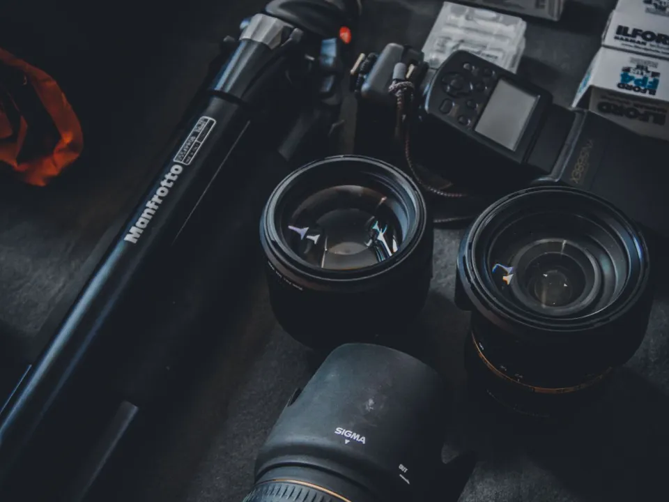Camera lenses, monopod, flash and film boxes laid out on dark fabric