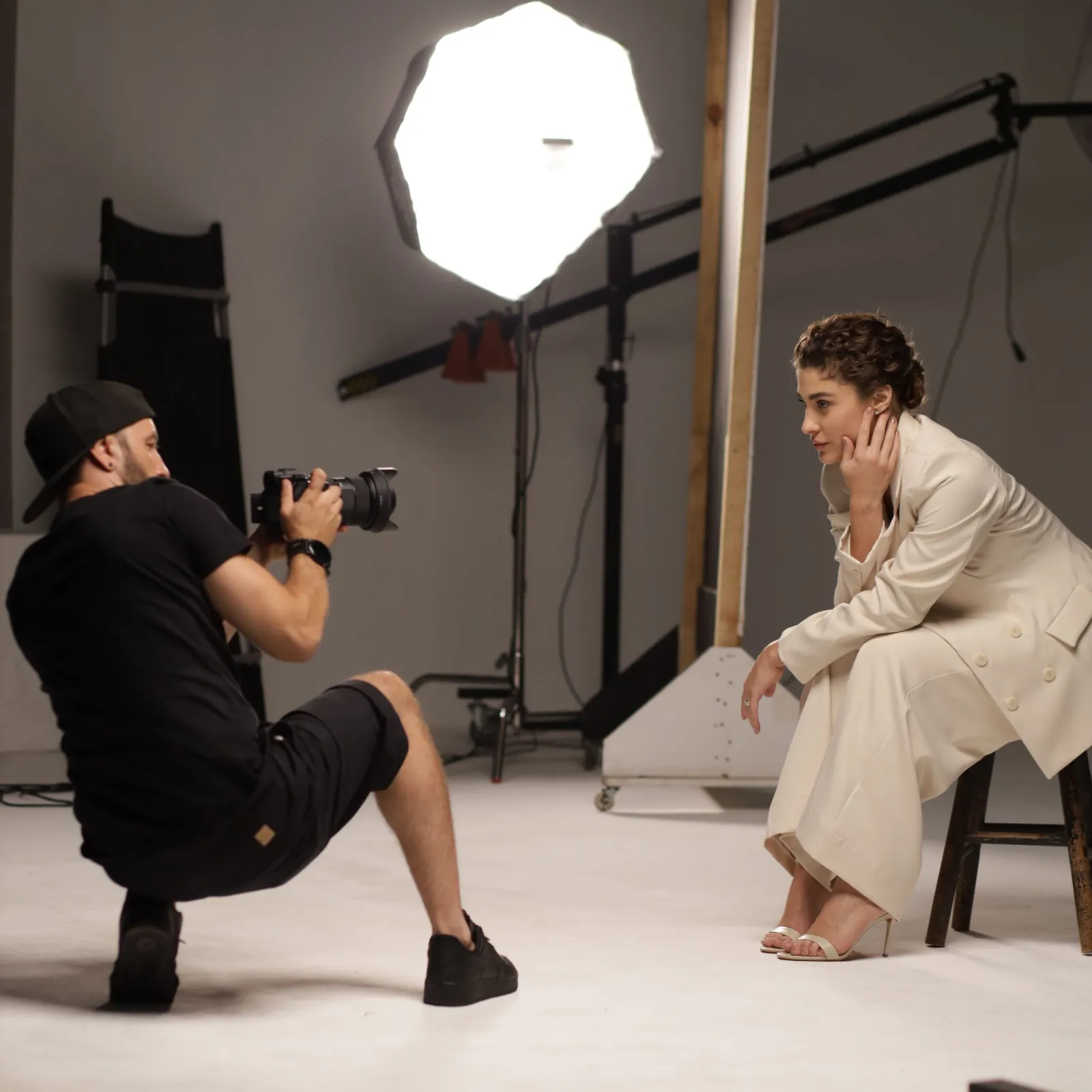 Photographer crouching to shoot a seated model under an octabox in a gray studio