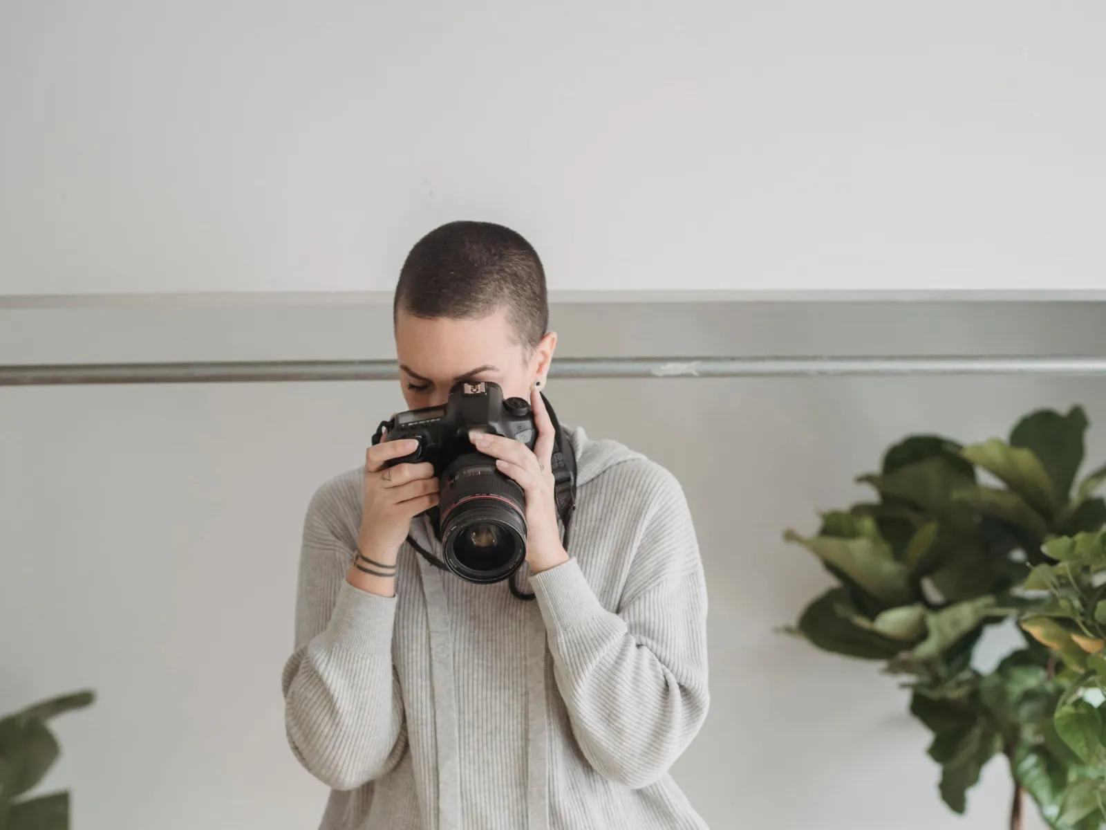 Photographer raising a DSLR to eye level in a bright studio with plants and gold tinsel