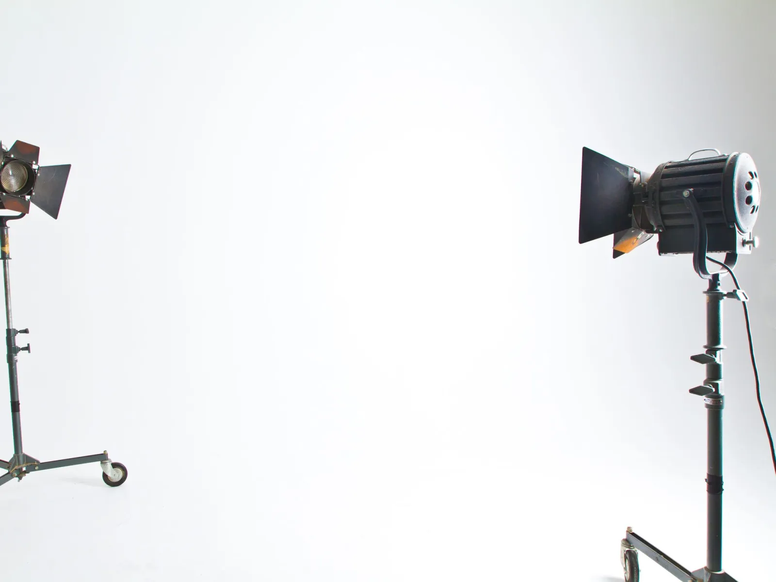 Two fresnel studio lights on rolling stands facing an empty white backdrop