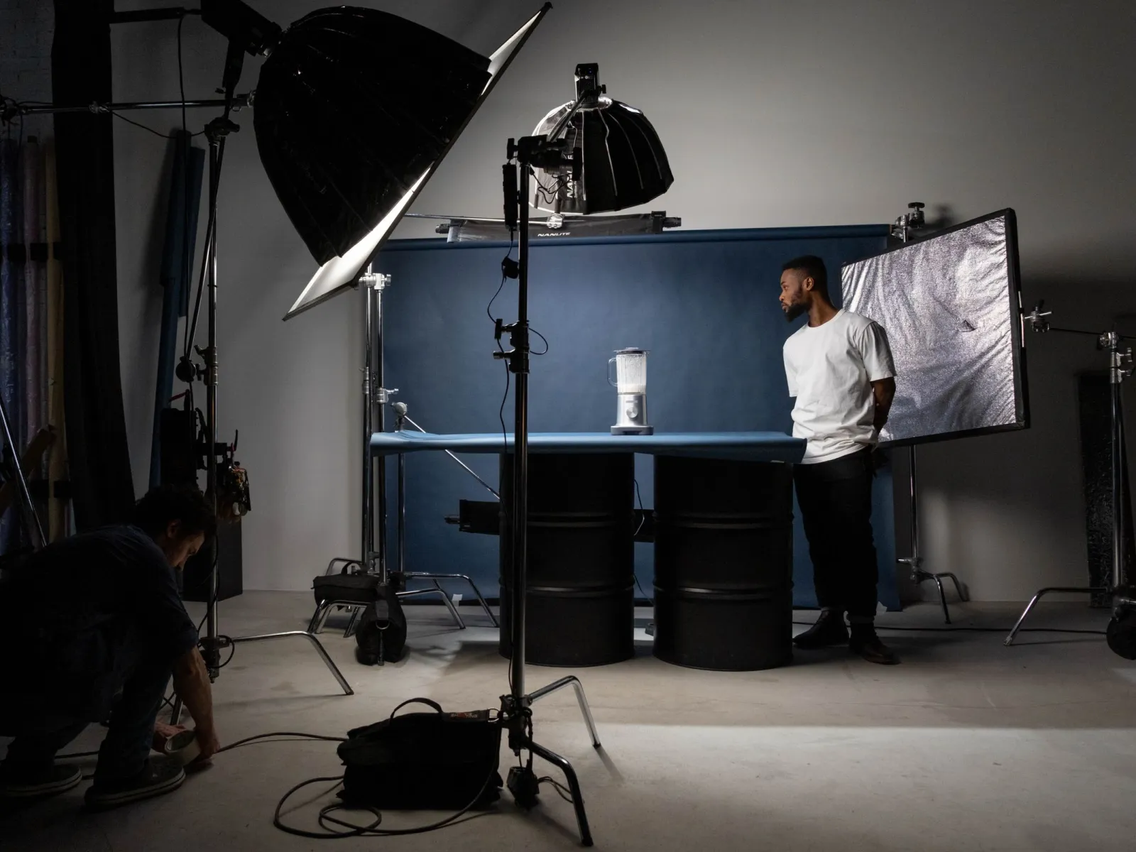 Crew preparing a product shoot with softboxes, a model and a blender on a blue tabletop set